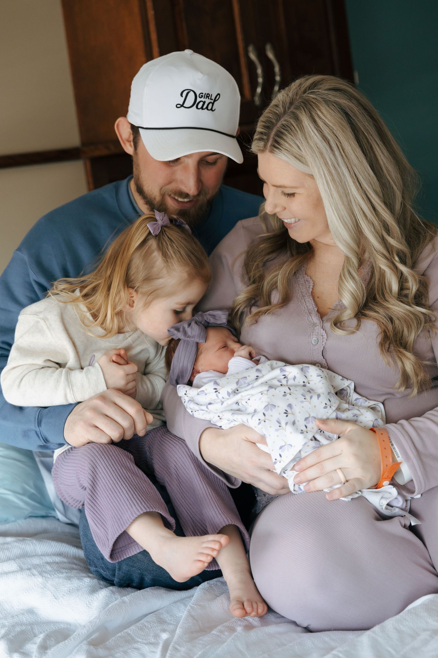 Happy family with a toddler and newborn baby poses together on a bed for a fresh 48 session.