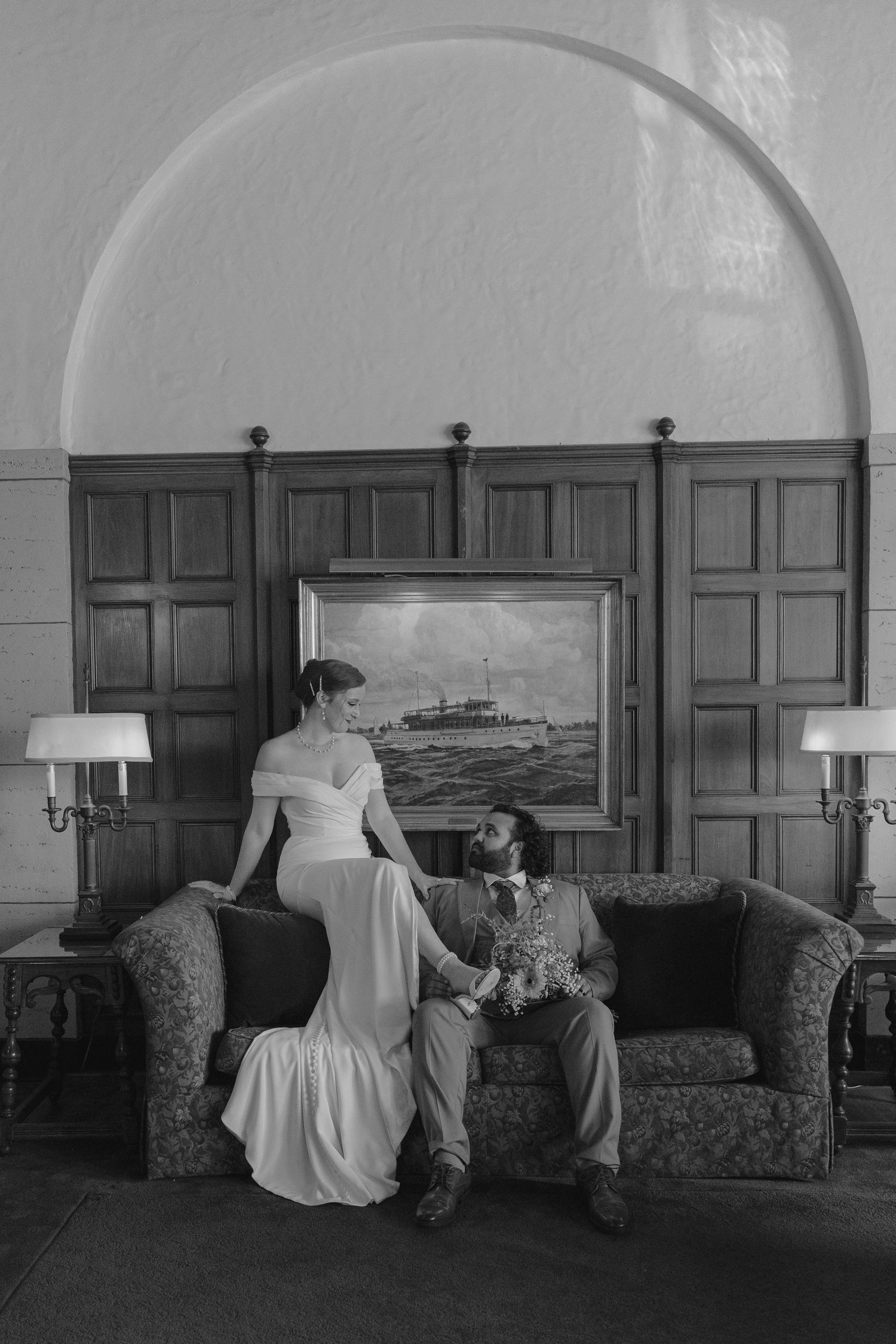 Bride and groom share a romantic moment on a vintage sofa in an elegant wood-paneled room.