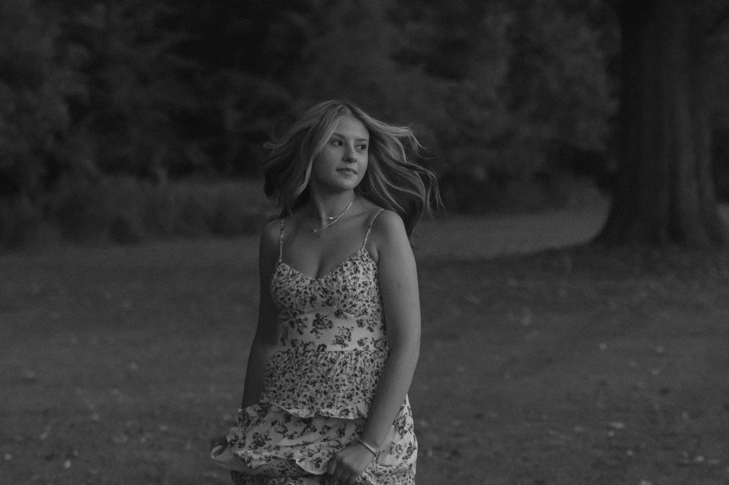 Black and white portrait of a young woman with flowing hair in a floral dress outdoors.