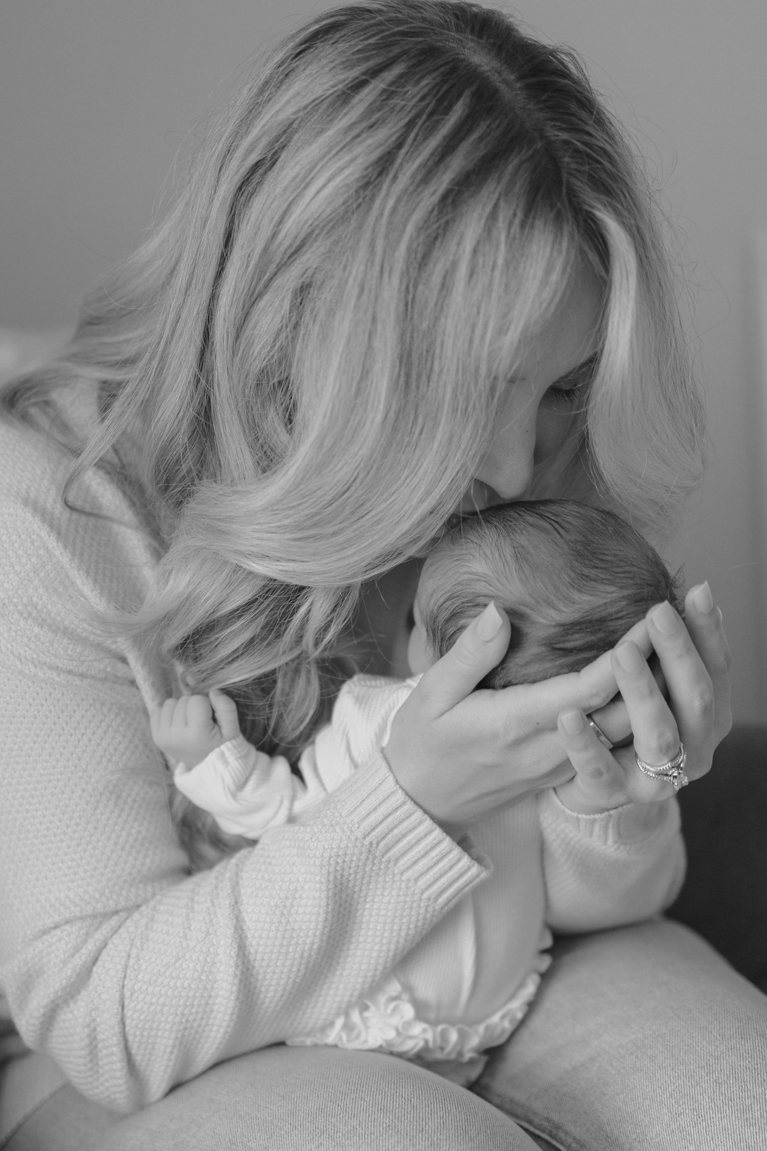 Black and white photo of blonde mother gently kissing her newborn baby while cradling them.