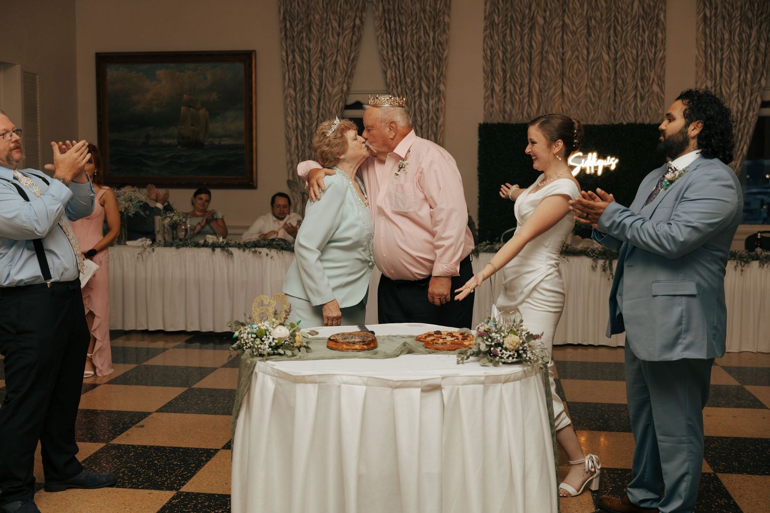 Wedding guests applaud as older couple shares a kiss during romantic wedding reception celebration.