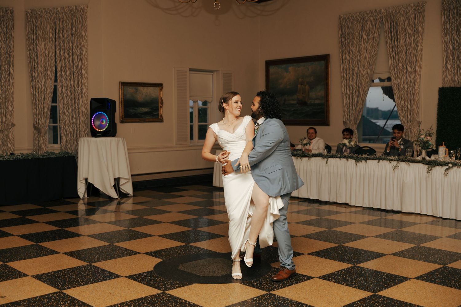 Couple sharing intimate first dance at elegant wedding reception with guests seated at head table.