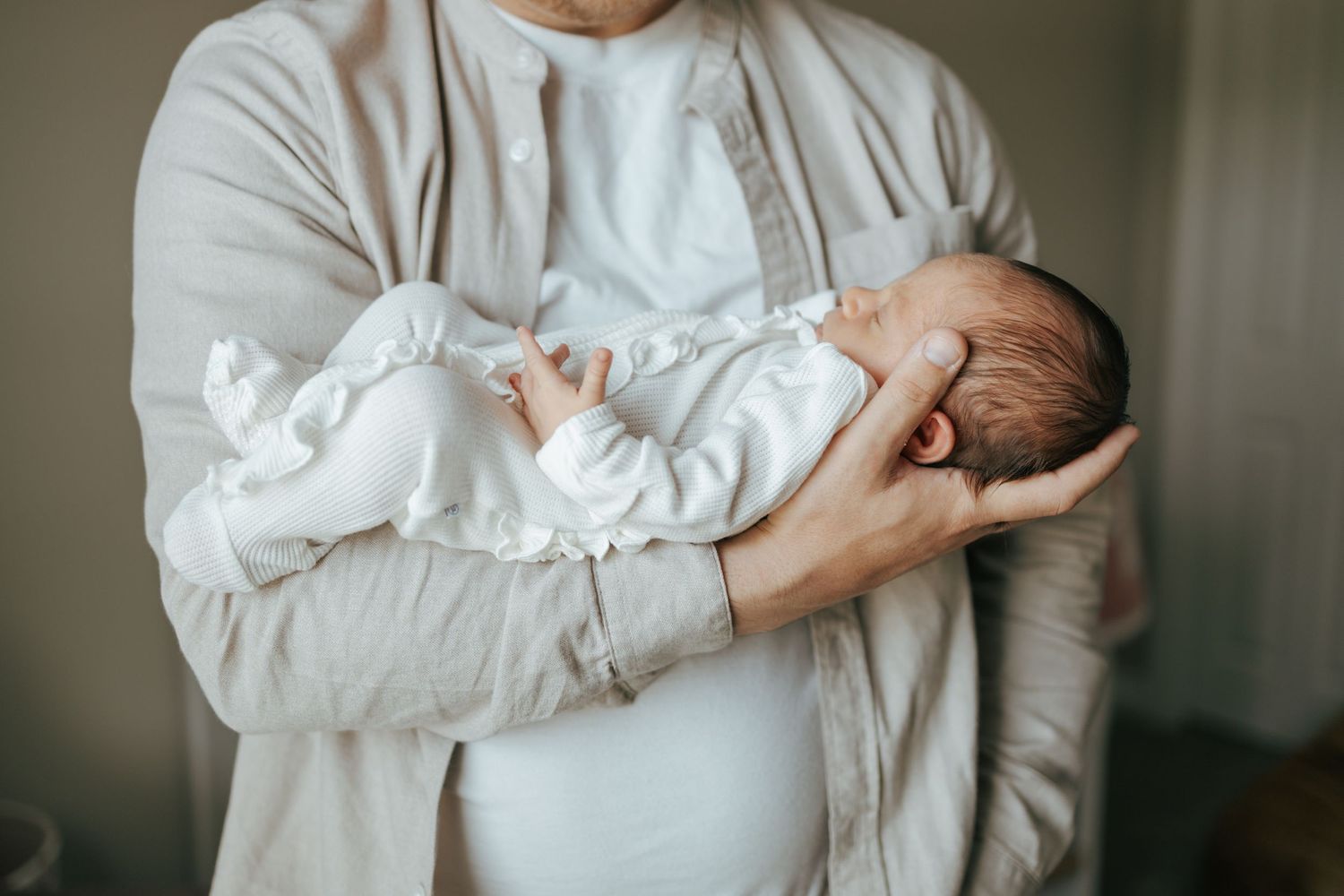 Close-up of father carefully cradling sleeping newborn baby in both arms against chest.