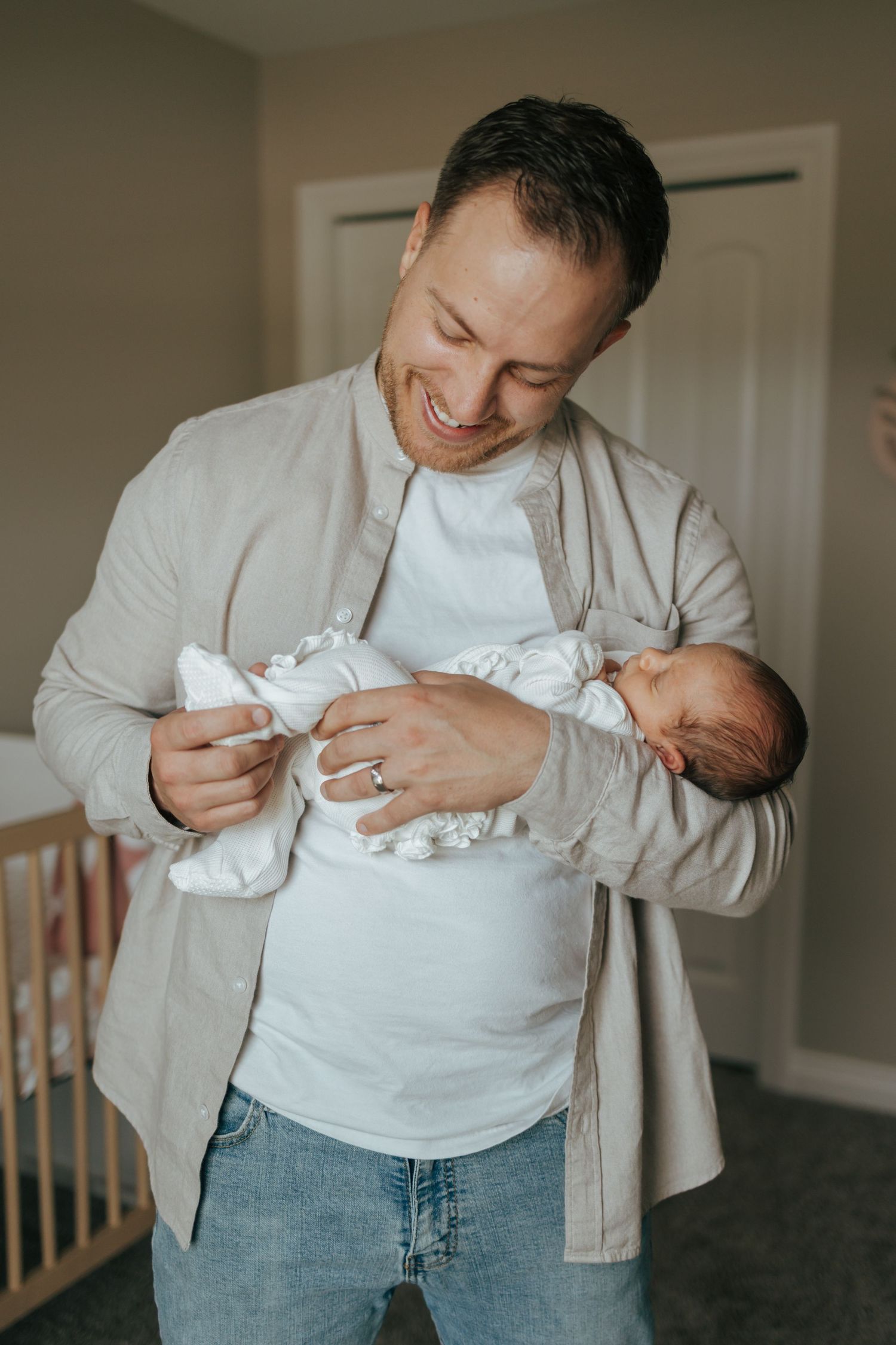 Happy father smiling down at his newborn baby while holding them in a nursery room.