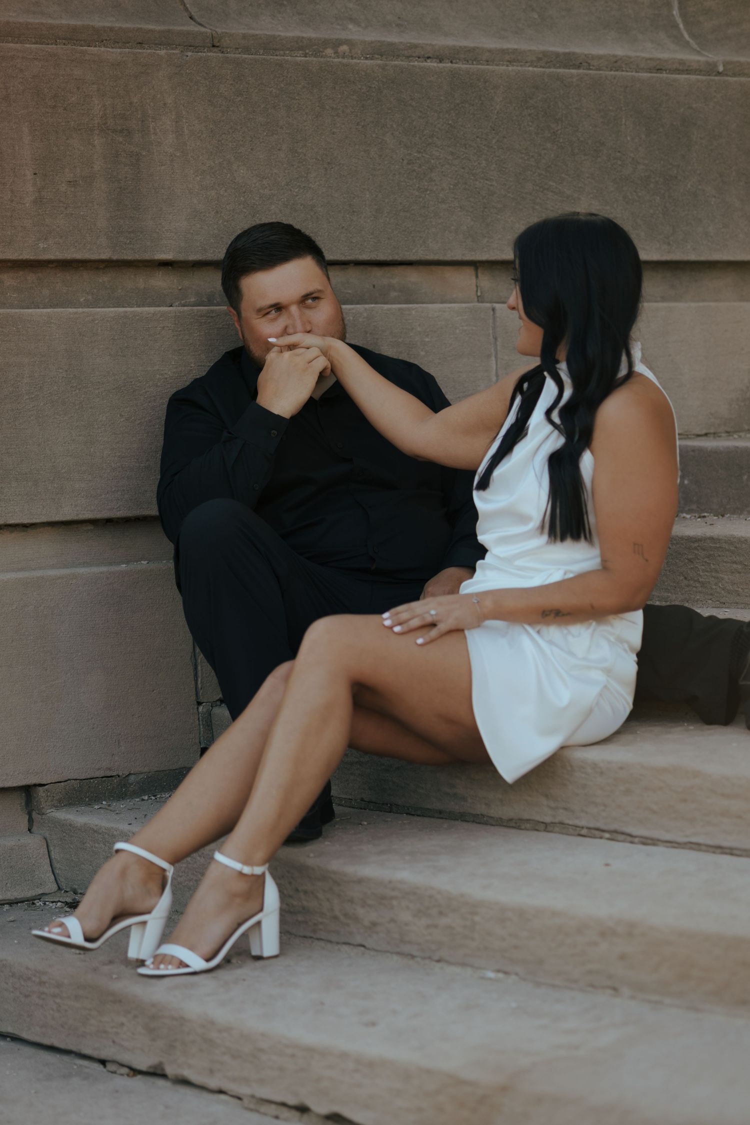 Woman extending her hand to man sitting on stone steps in an intimate engagement photo.