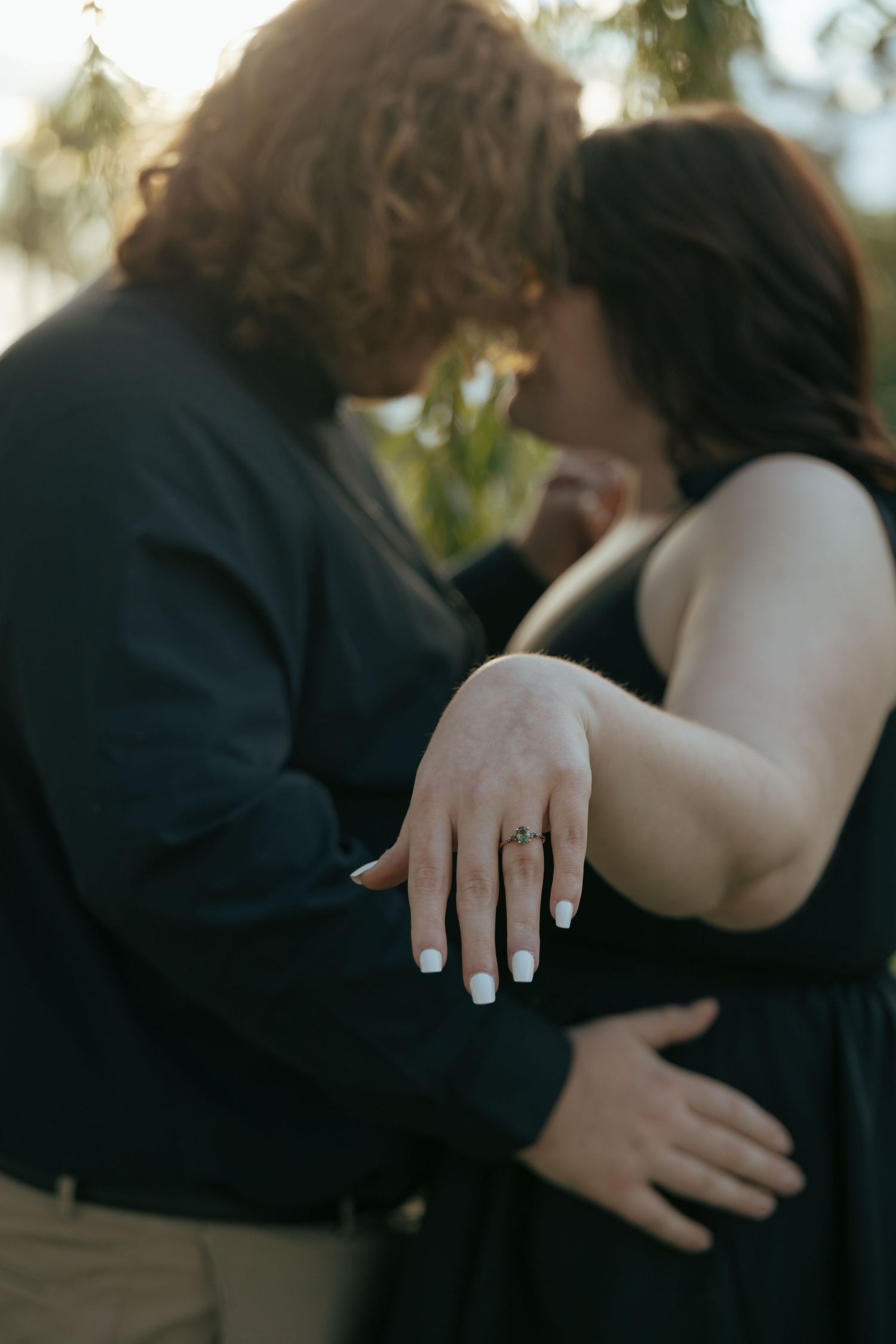 Engaged couple kissing while woman displays her diamond engagement ring.