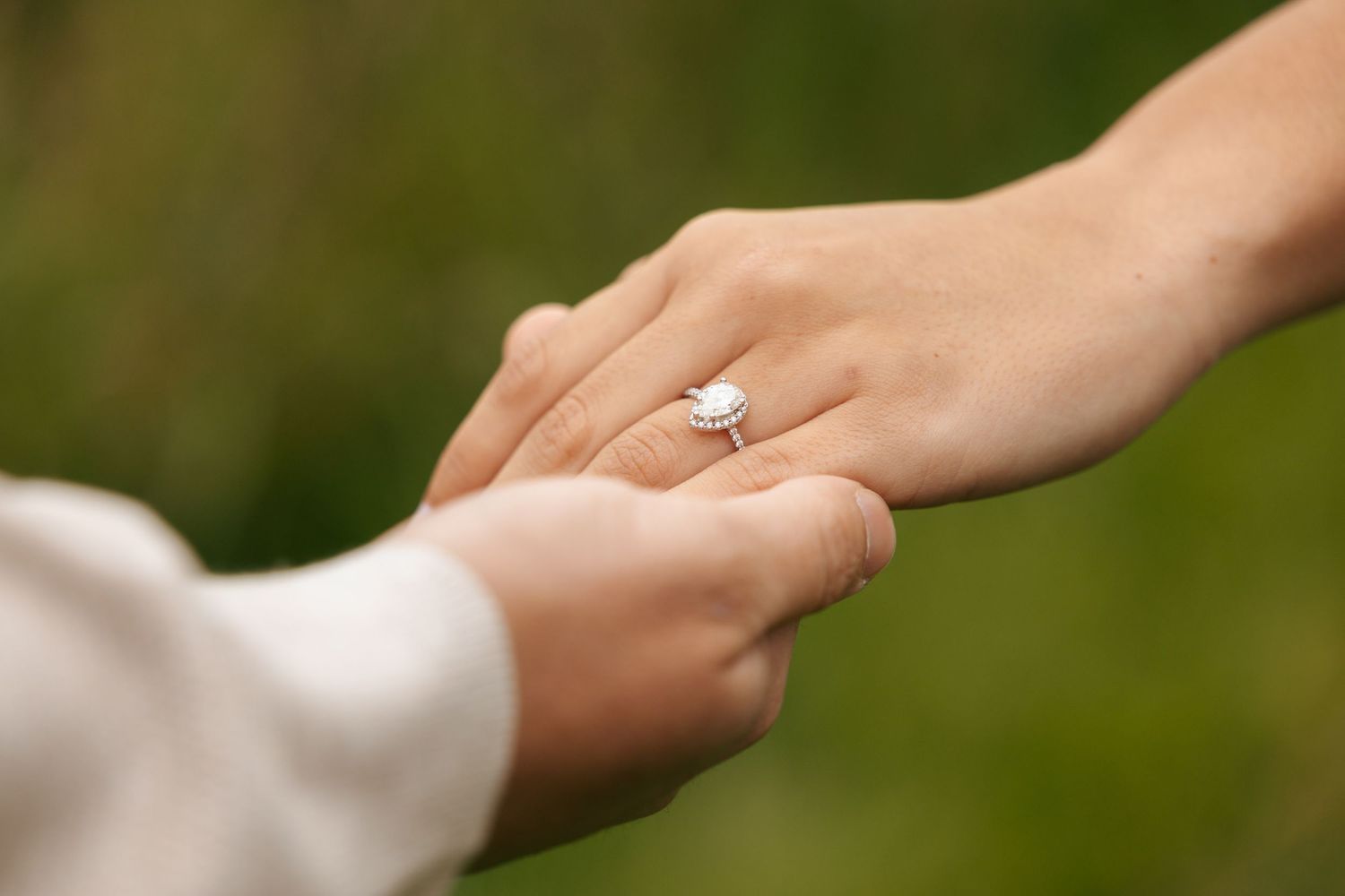Close-up of woman's hand displaying oval diamond engagement ring while holding partner's hand.