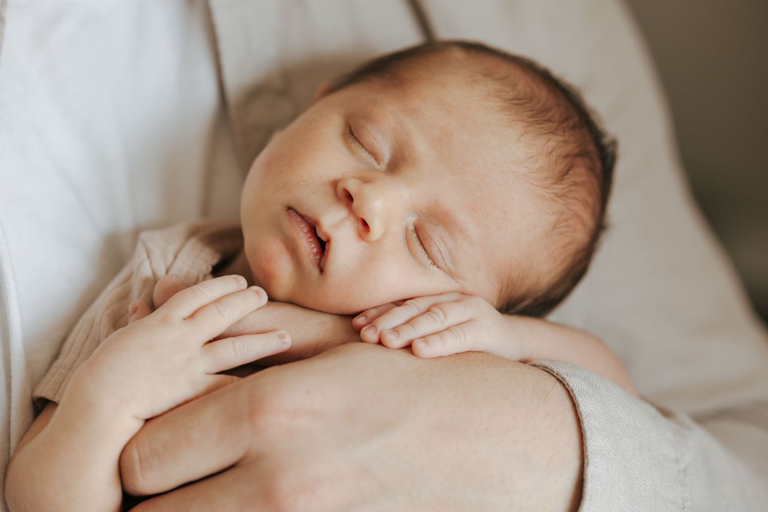 Peaceful sleeping newborn baby resting on a parent's chest with tiny hands folded.