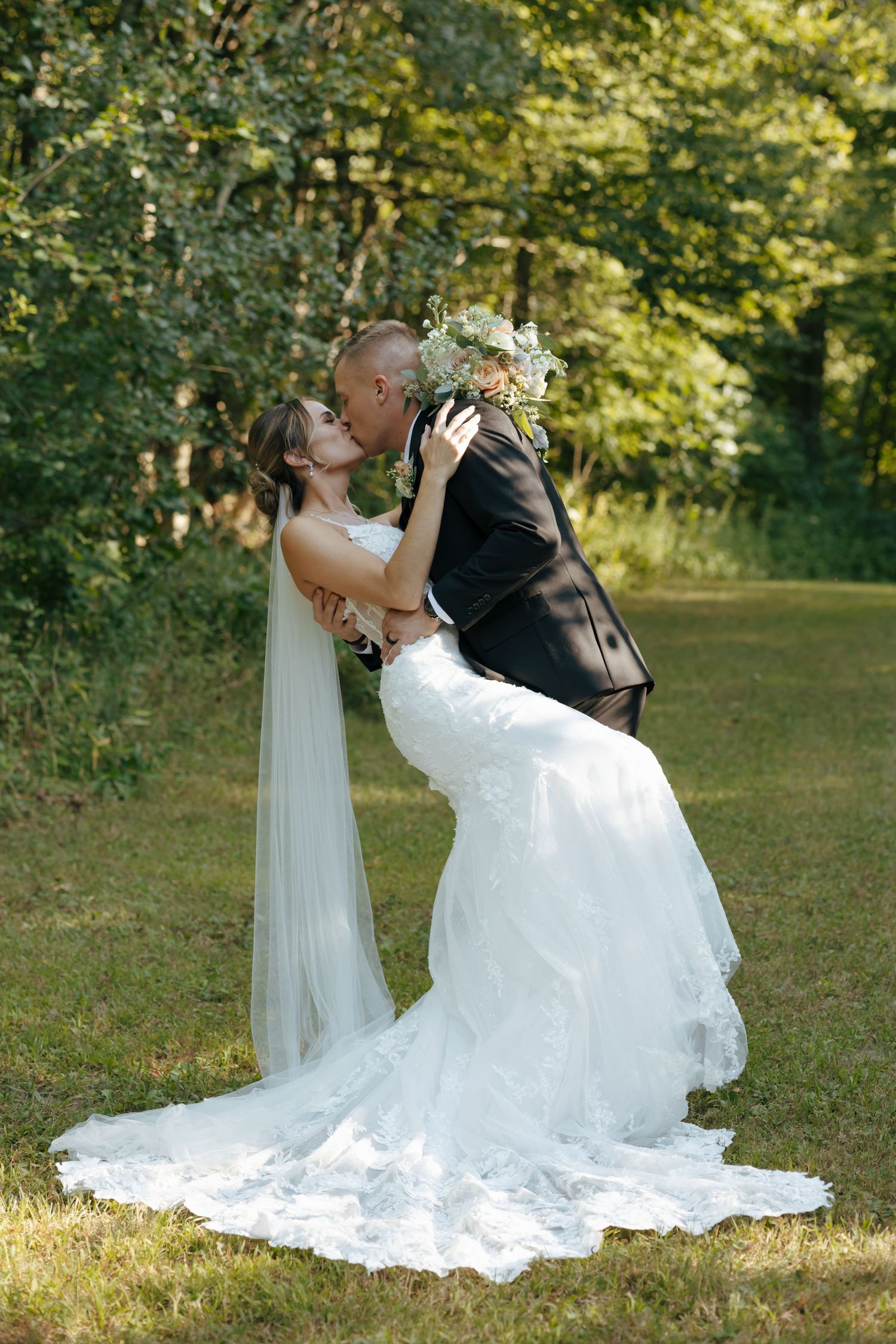 Bride and groom sharing a romantic kiss outdoors in a lush green garden setting.