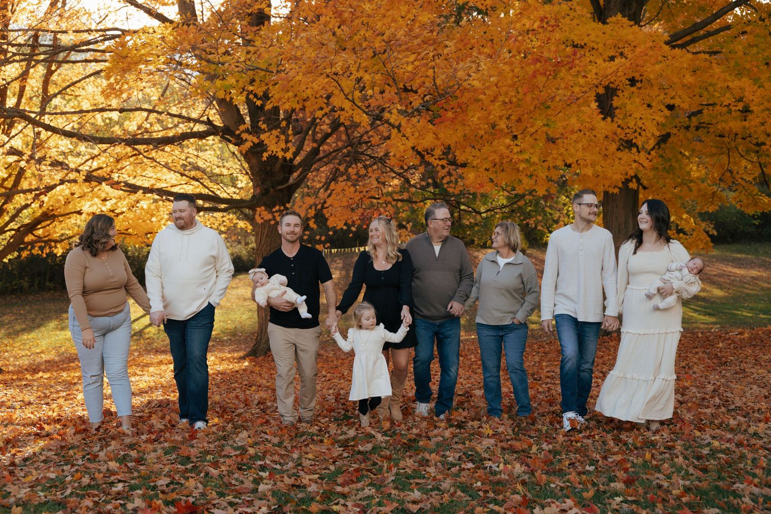 Large family portrait among vibrant orange autumn foliage in a park.