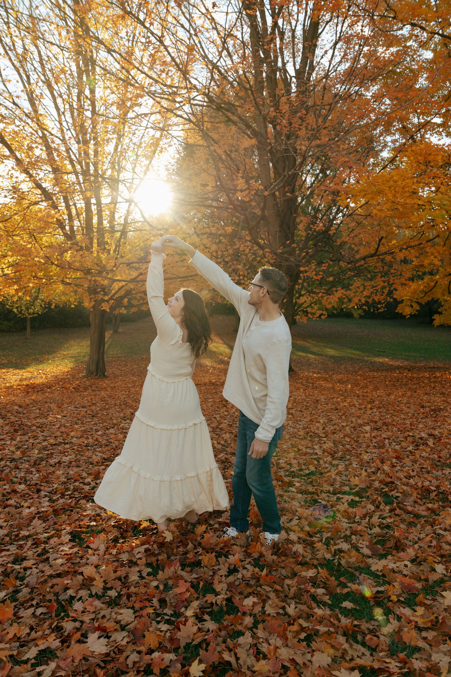 Couple dancing and spinning in a sun-drenched autumn leaf-covered park.