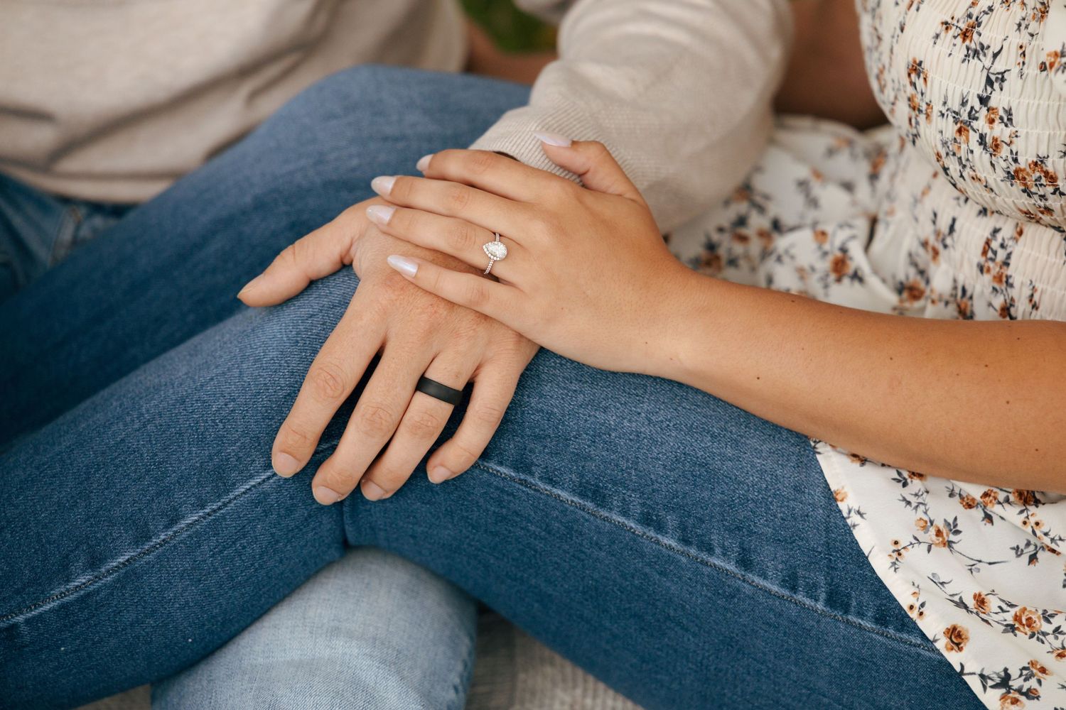 Close-up of a couple holding hands showing an engagement ring, woman wearing floral top and jeans.