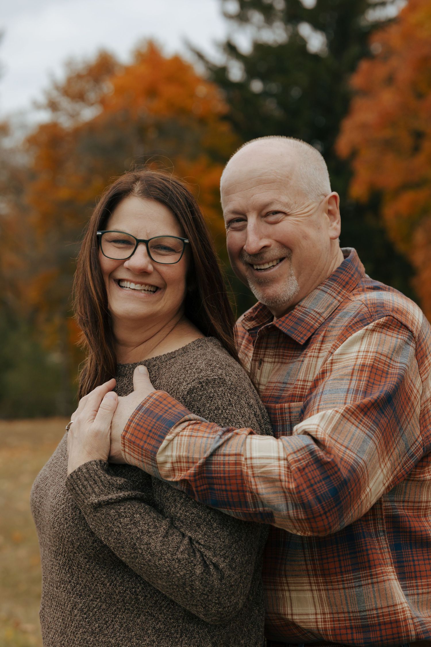 Happy couple embracing outdoors with vibrant orange and red autumn foliage in background.