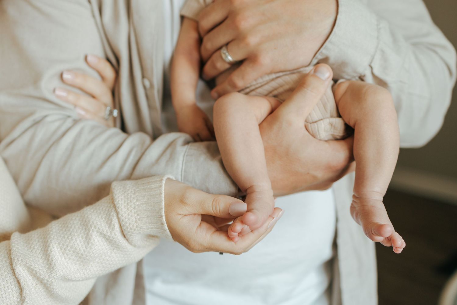 Close-up of new parents hands holding their newborn babys tiny feet and body together.
