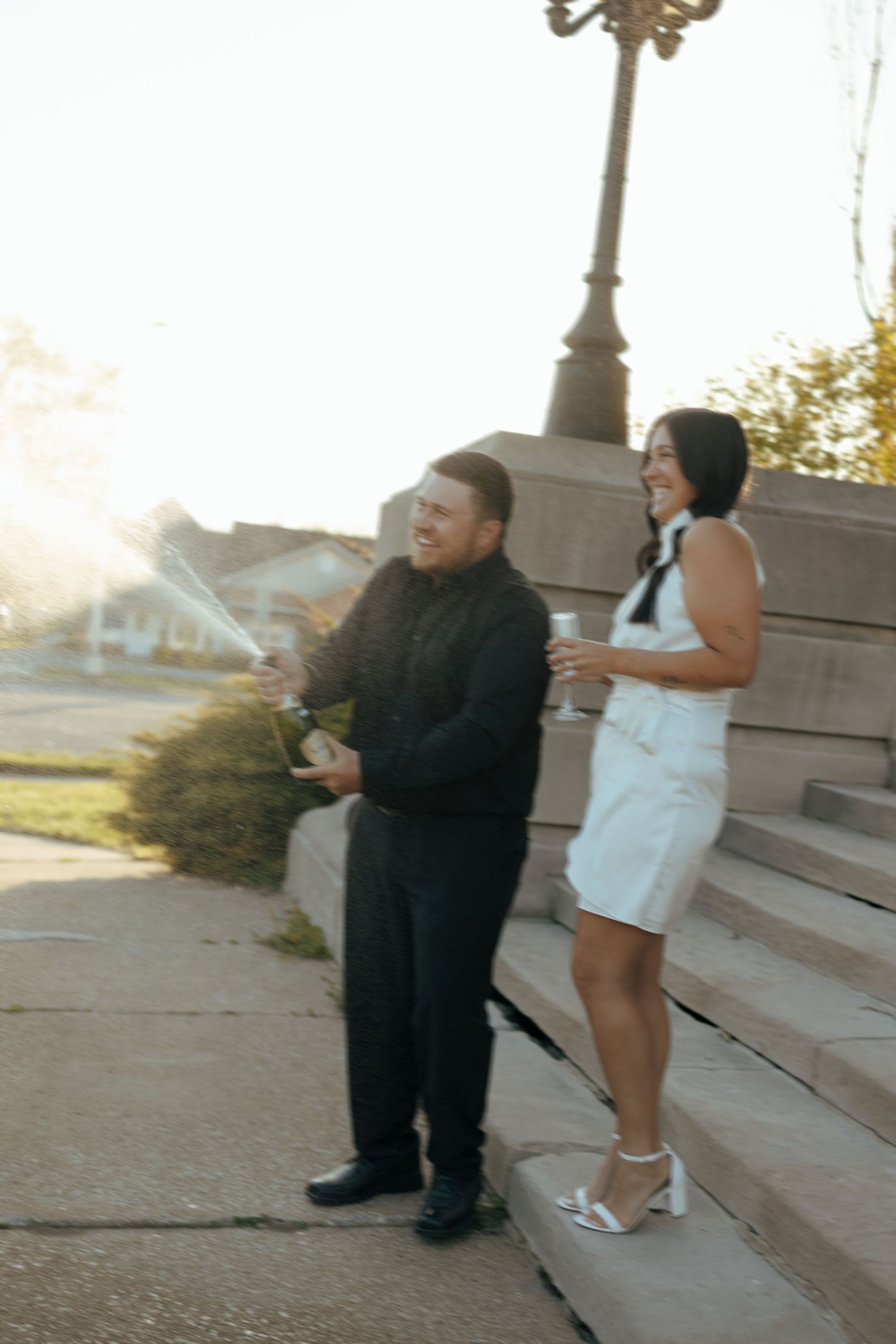 Joyful couple popping champagne on outdoor steps at golden hour to celebrate their elopement.