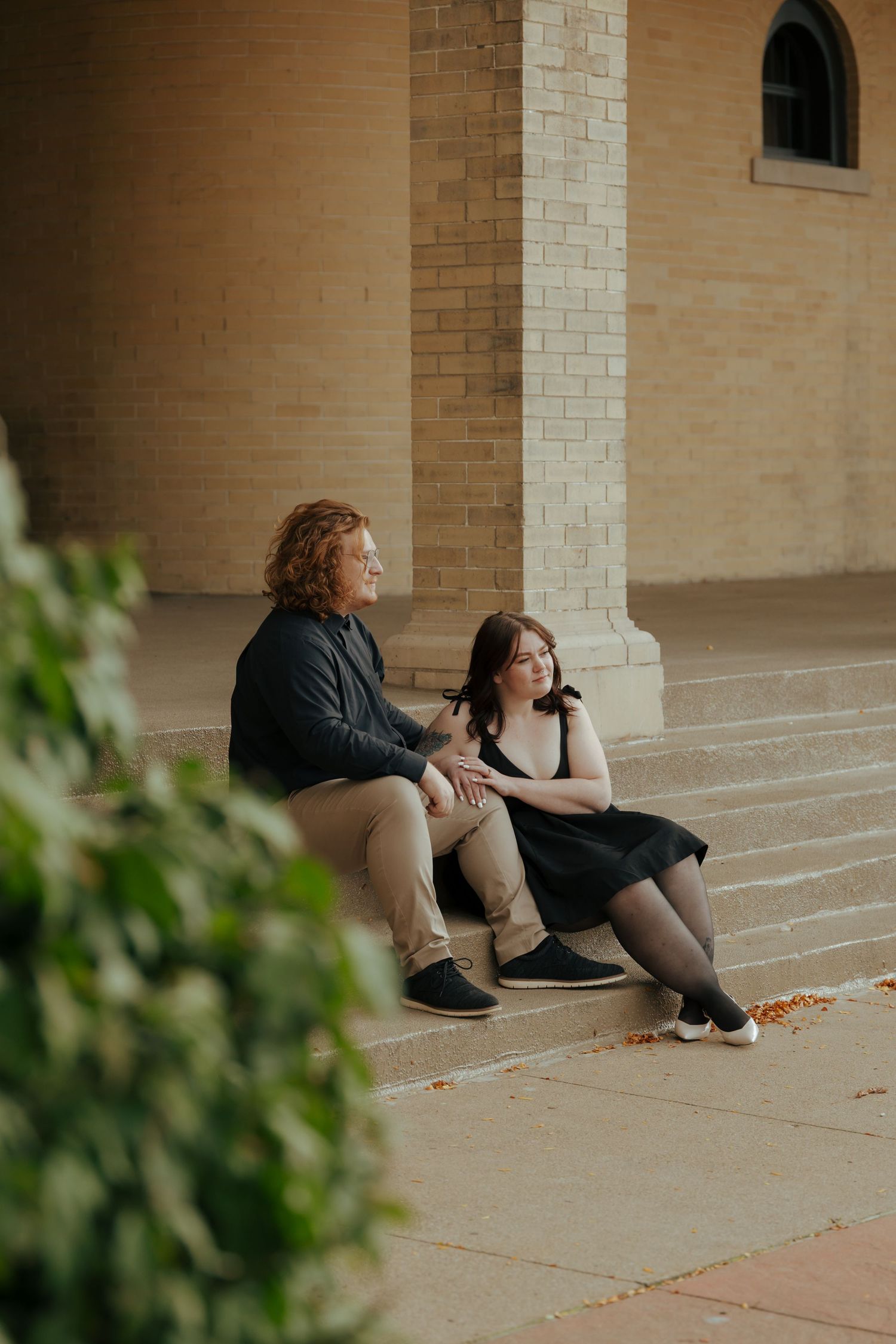 Couple sitting on stone steps of a brick building in casual conversation.