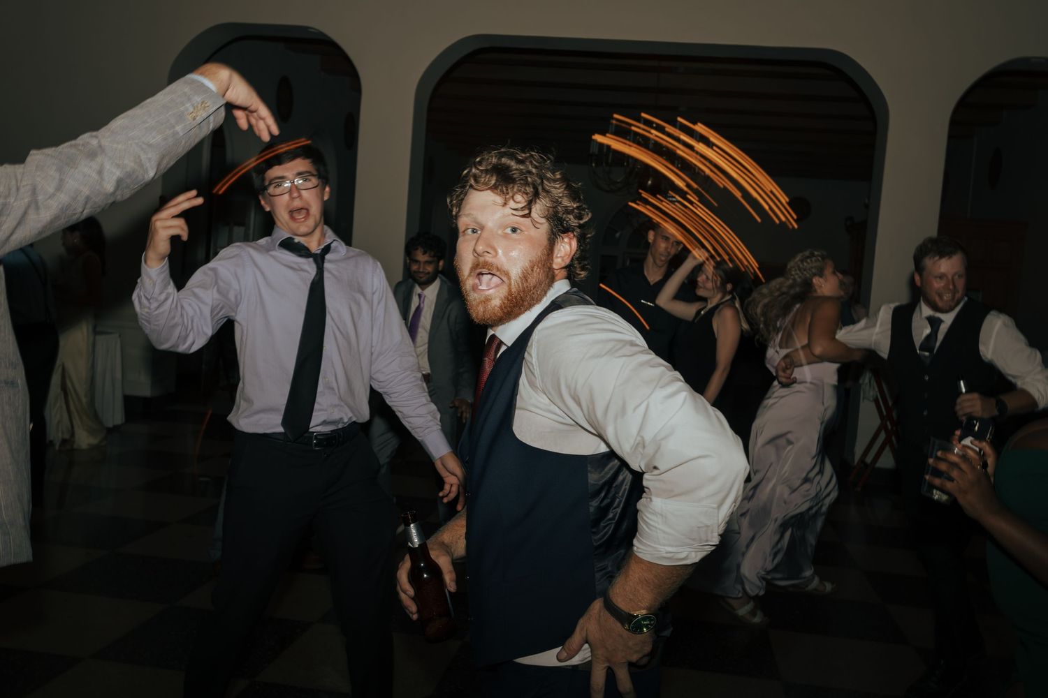 Groomsmen dancing energetically at wedding reception with light trails in background.