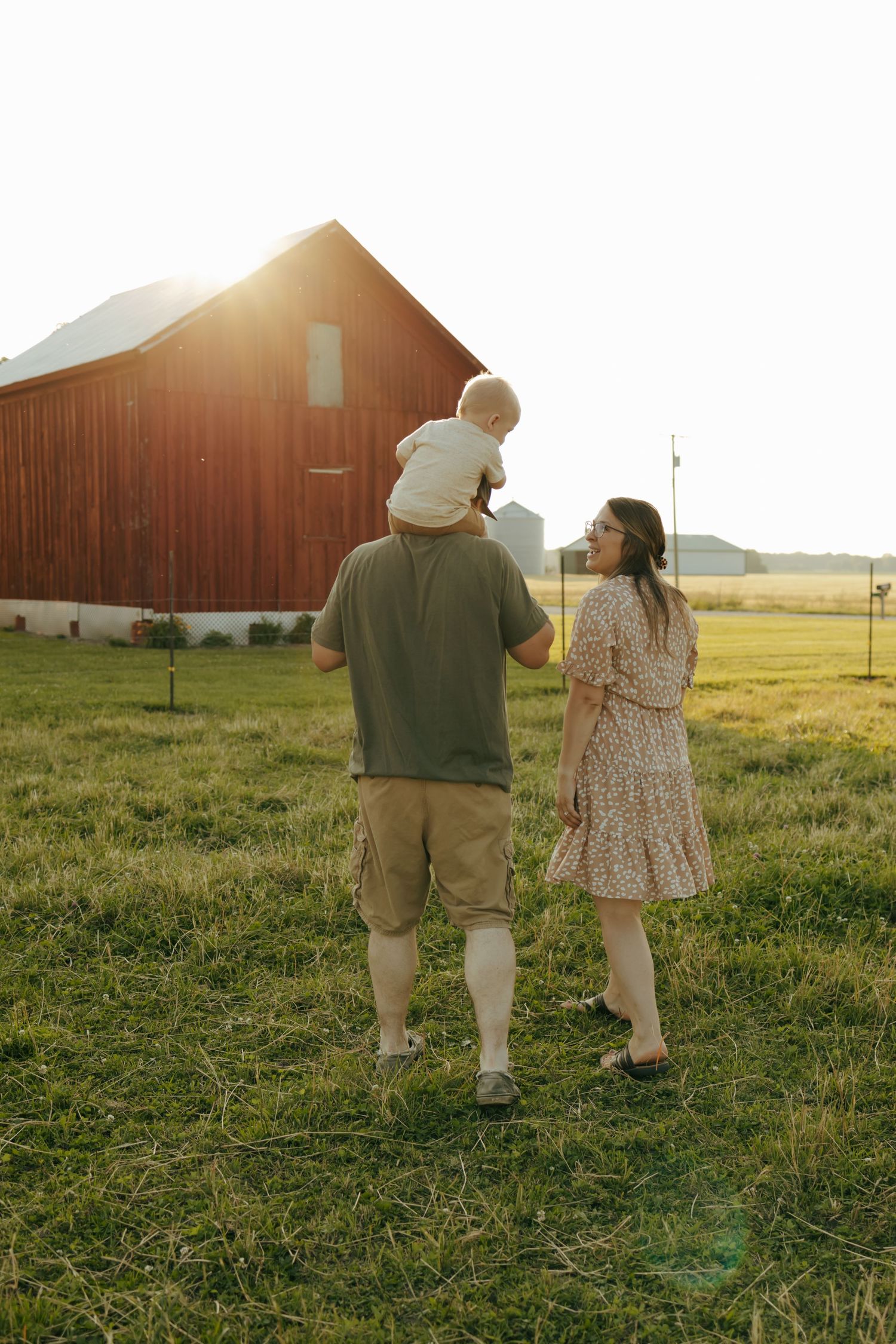 Family of three walking toward red barn at golden sunset on a farm property.