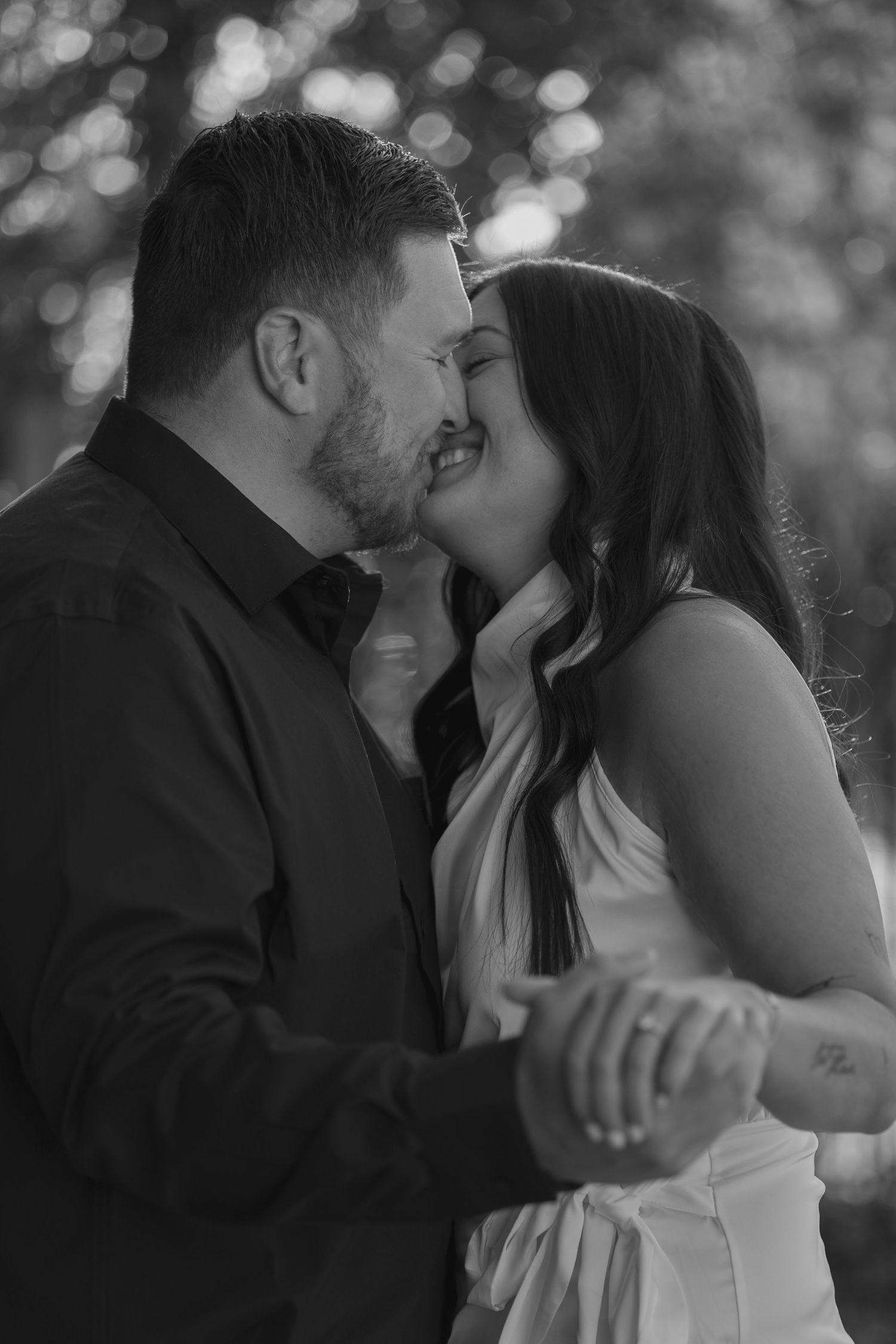 Black and white close-up of a couple sharing a kiss while holding hands outdoors.