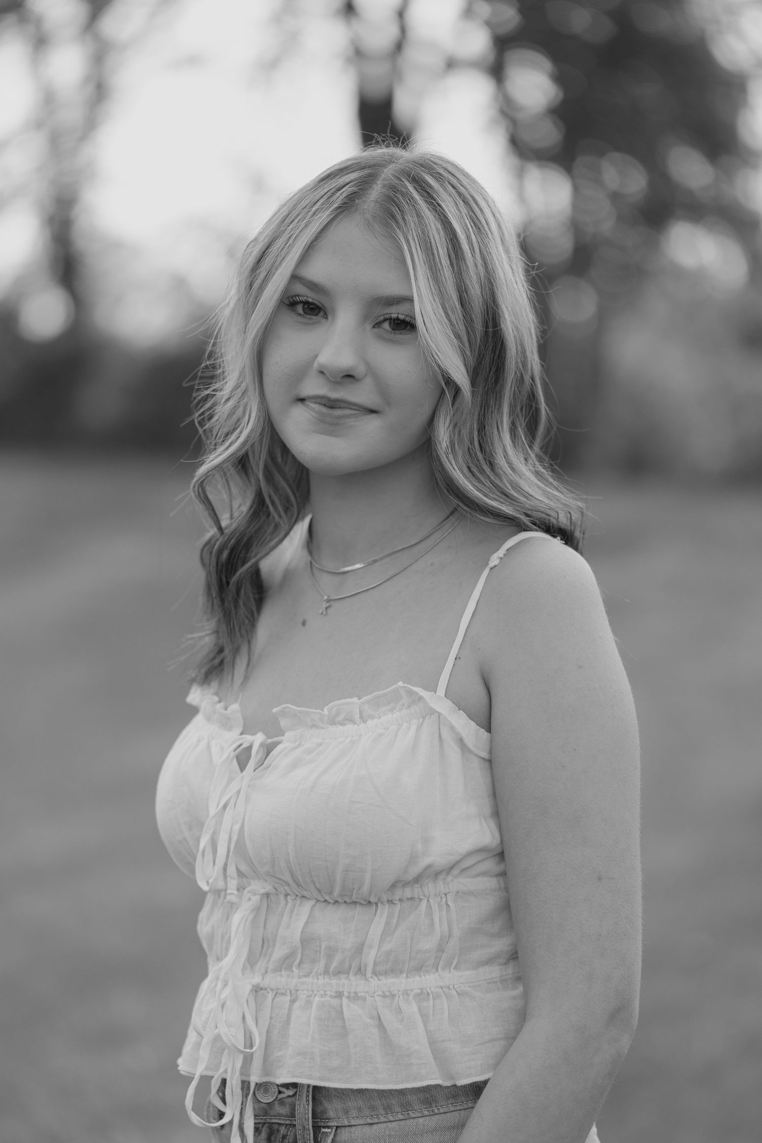 Black and white portrait of blonde teen girl in white ruffled crop top smiling softly outdoors in natural light.