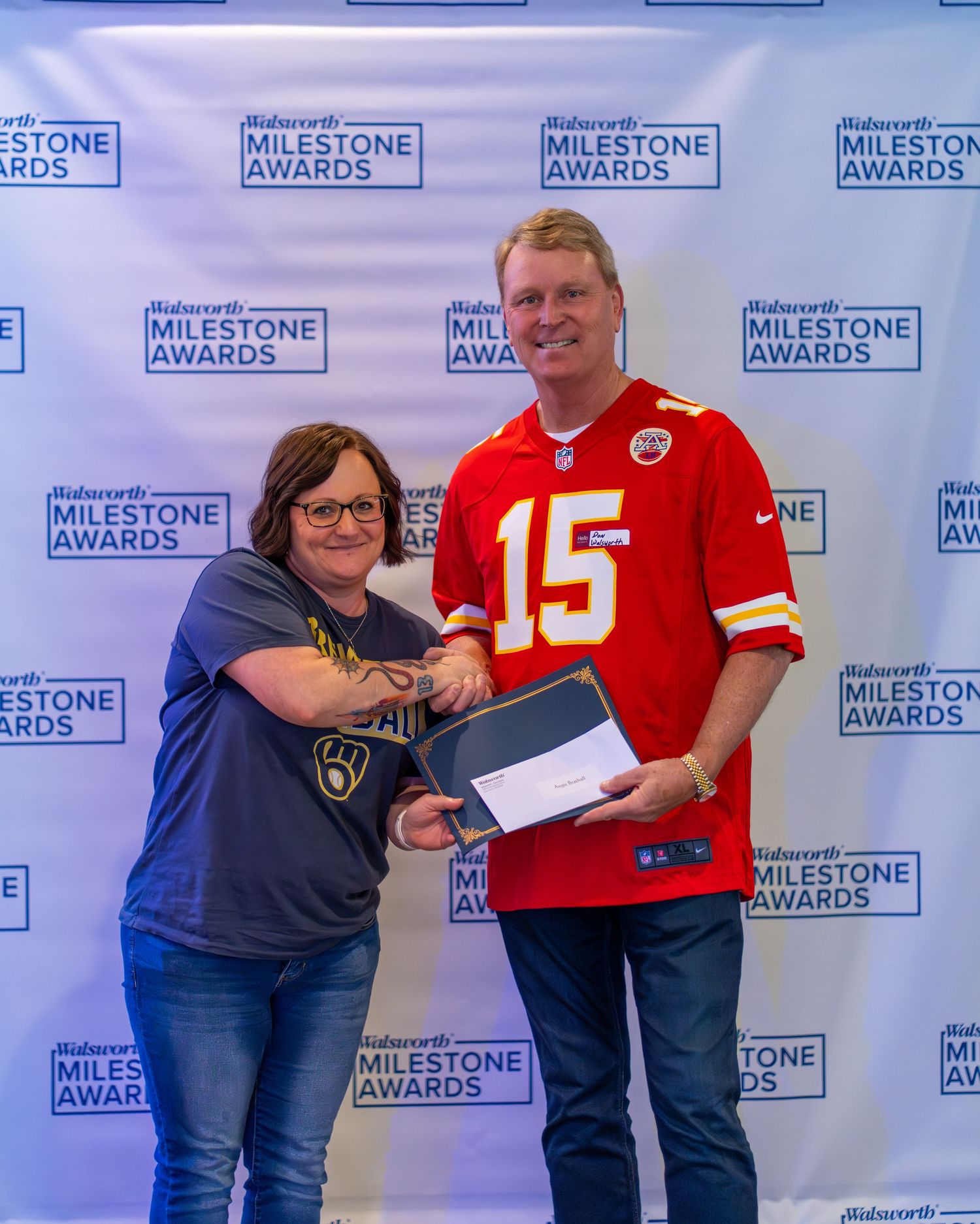 Several people in Kansas City Chiefs jerseys and casual wear stand in a row against a blue branded backdrop at an event.