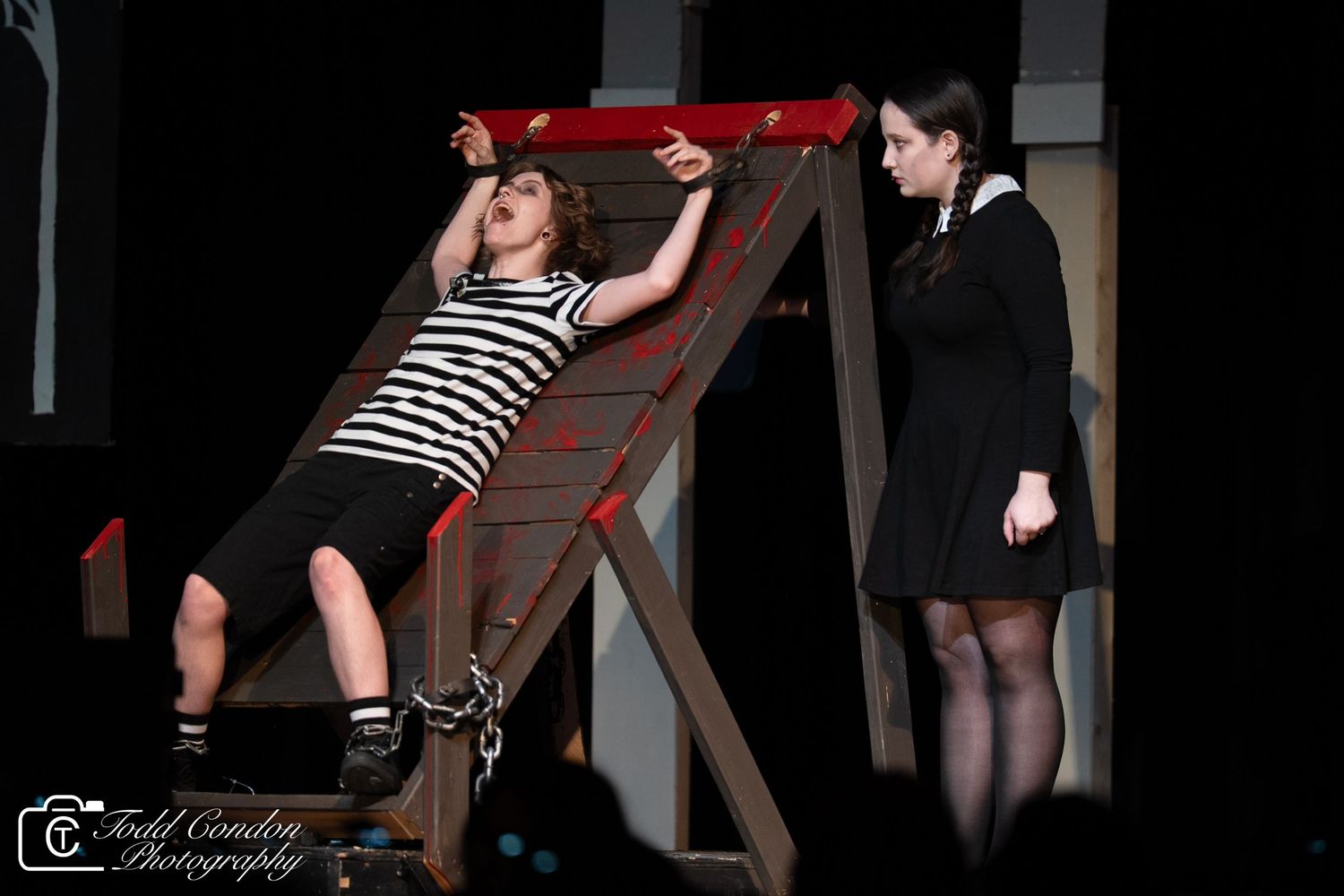 Dancers in black and striped outfits perform on red chairs during a dramatic stage performance.