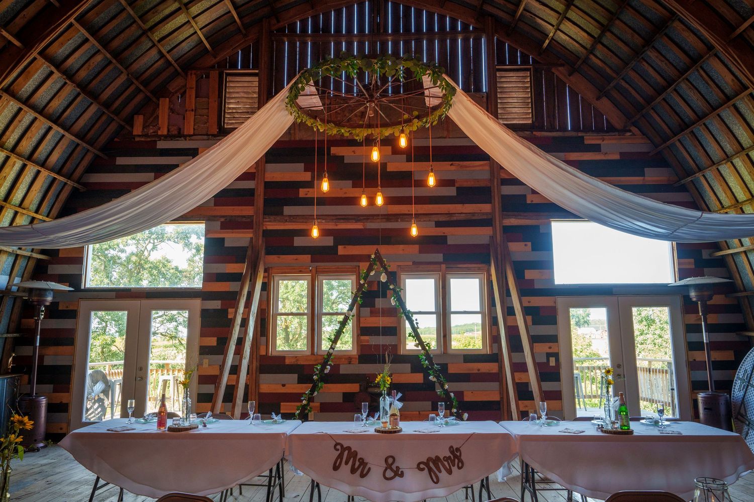 Rustic log cabin wedding venue interior with draped fabric, hanging lights and wooden beams overhead.