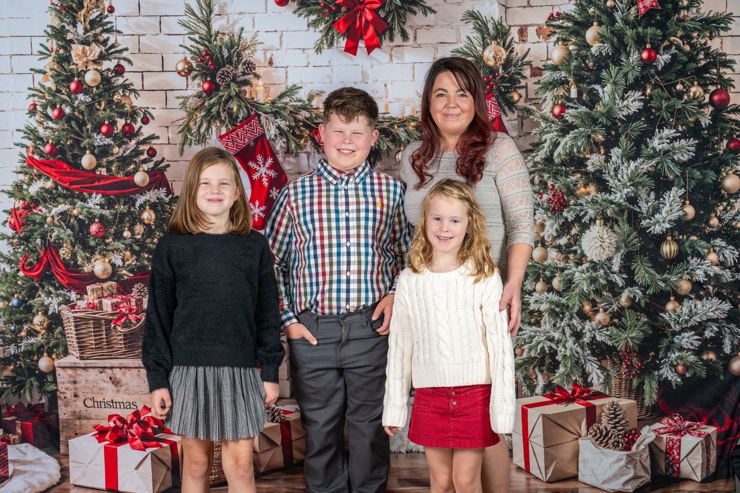 A group stands together in front of a decorated Christmas tree and white brick wall with wrapped presents.