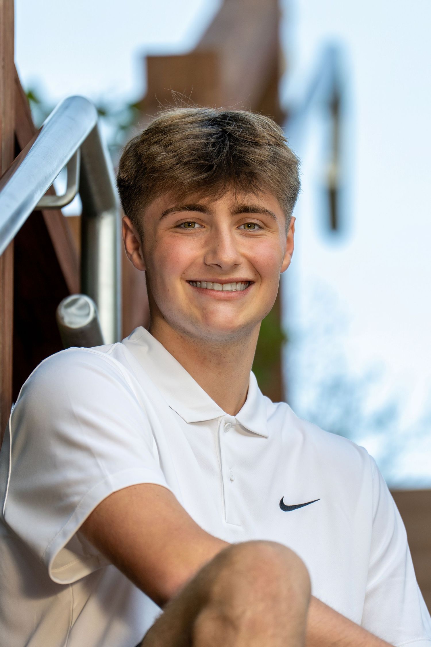 Young person in white Nike polo shirt smiling against blurred background.