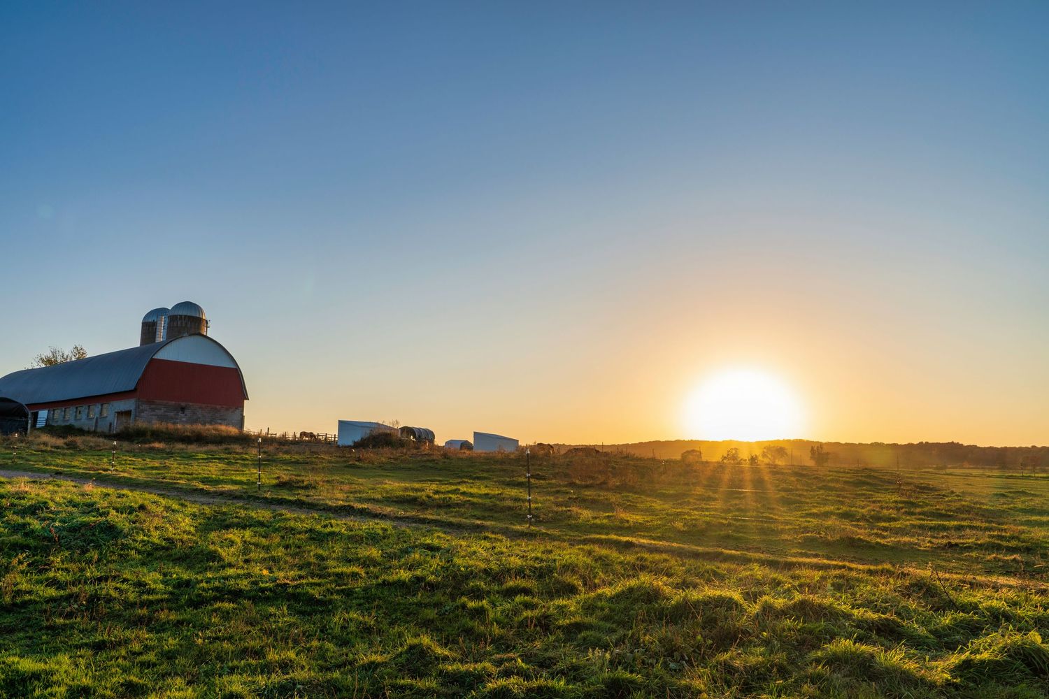 Red barn silhouetted against a dramatic sunset sky on rolling farmland.