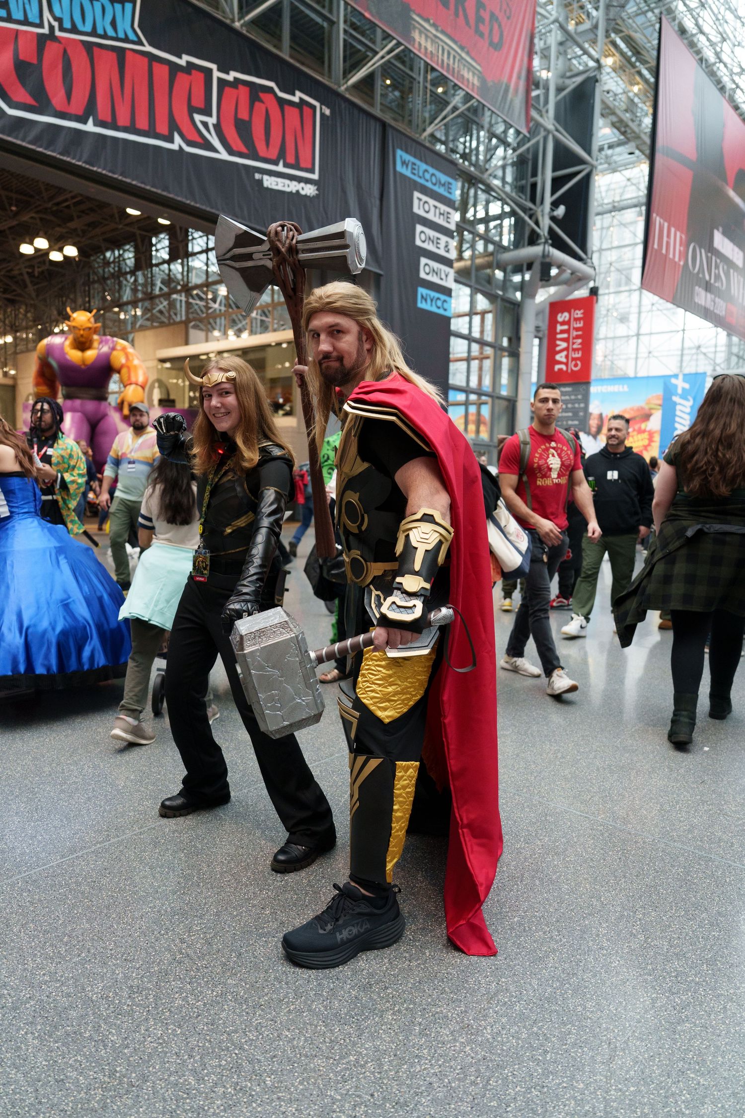 Two Thor cosplayers pose with hammers at New York Comic Con in a busy convention hall.