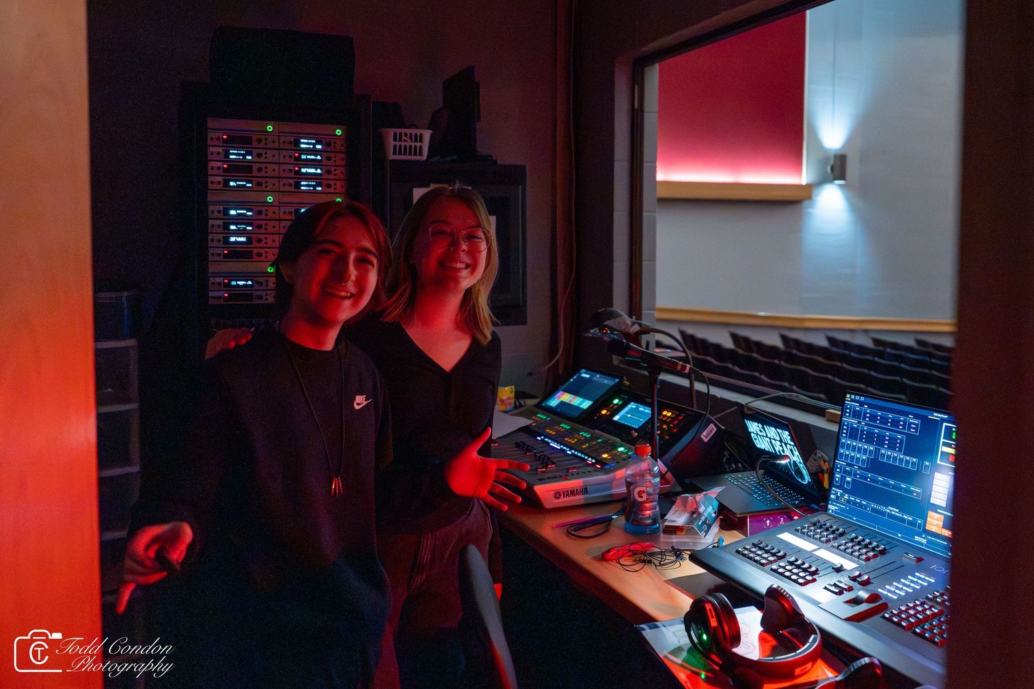 Audio engineers work at a professional mixing console in a dimly lit recording studio with red ambient lighting.