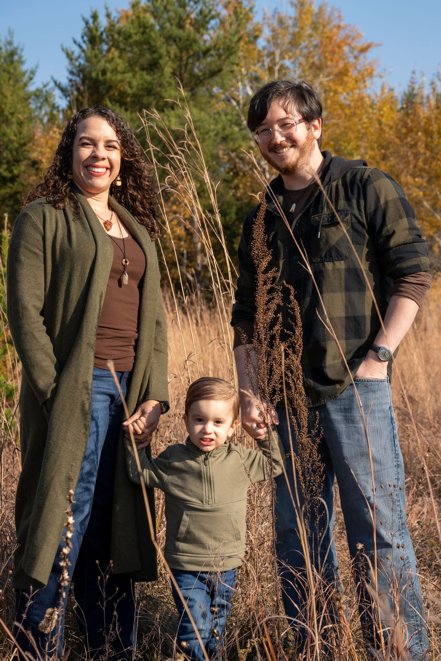 A happy family enjoying autumn weather together among tall grass and fall foliage.