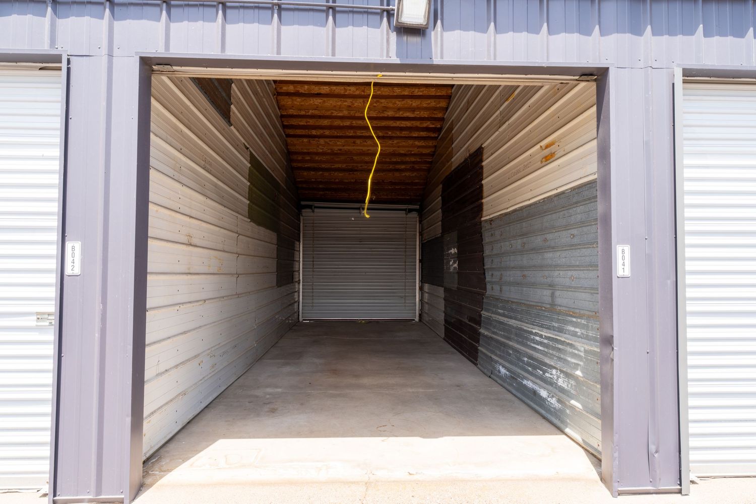Long empty storage unit hallway with white walls and roll-up doors visible in a self-storage facility.