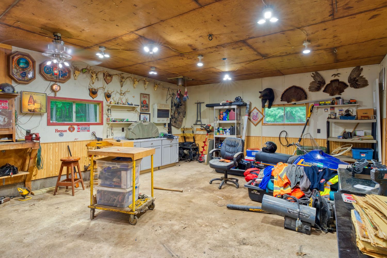Rustic workshop garage with wood ceiling, workbench, recessed lighting, tools on walls, and equipment on concrete floor.