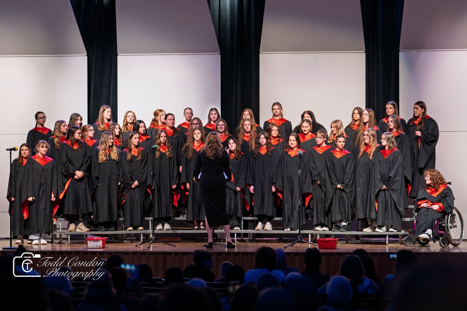 A choir group performs on stage wearing black robes with red accents during a formal concert performance.