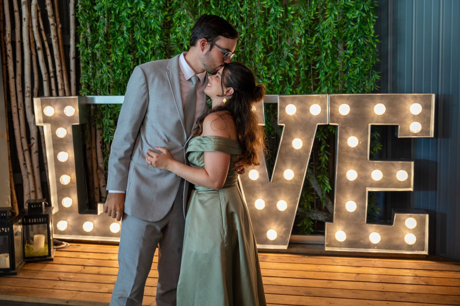 Couple shares romantic moments in front of illuminated marquee letters at outdoor wedding venue.