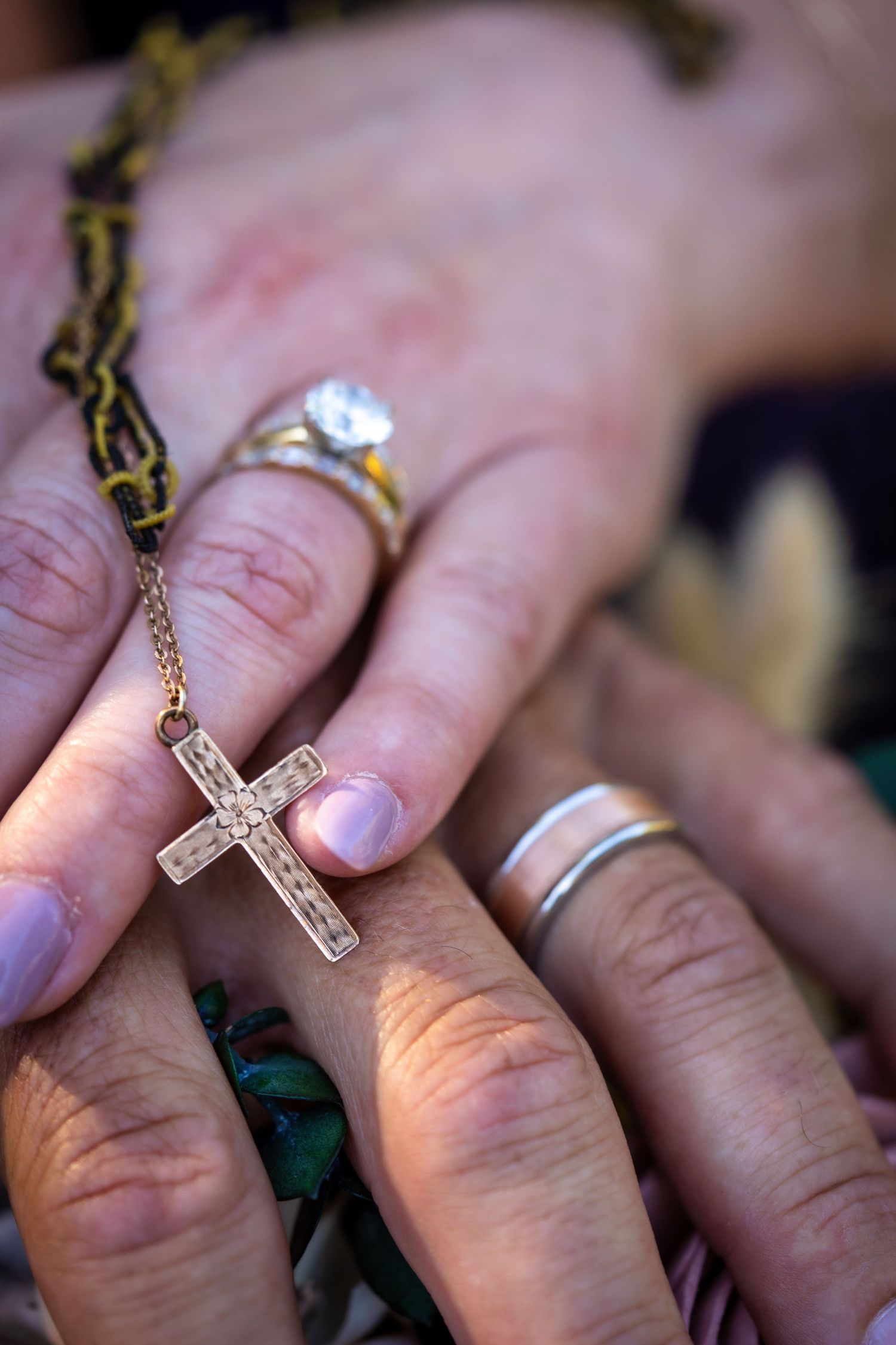 Close-up series of photos showing a gold cross pendant on a chain being held against someone's hand with a silver ring.
