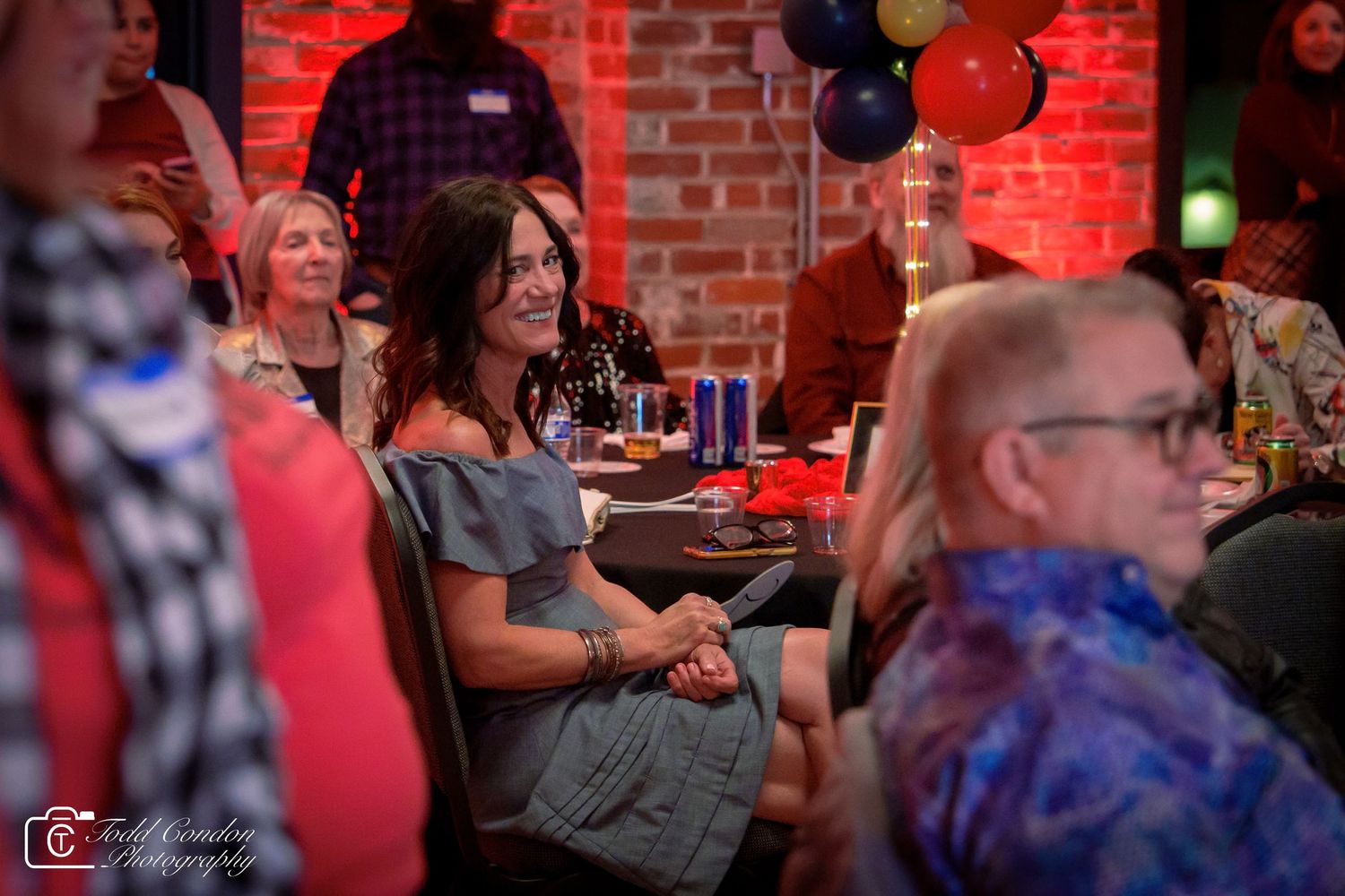Woman smiling and laughing at a festive indoor party with colorful balloon decorations in background.