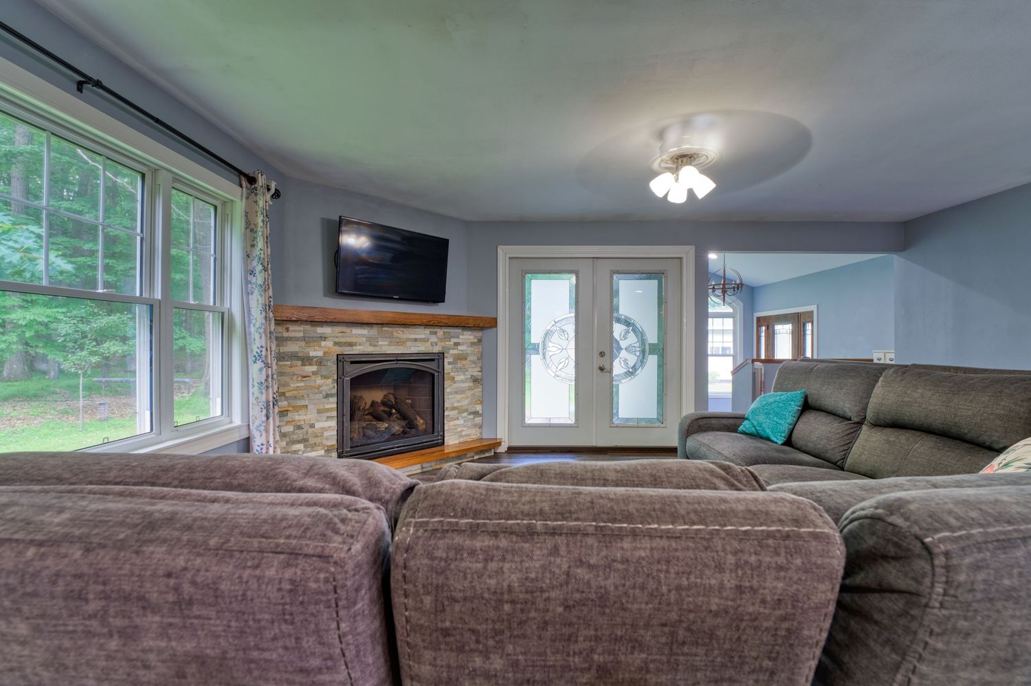 Cozy living room with stone fireplace, large sectional sofa, French doors, and a wall-mounted TV near bright windows.