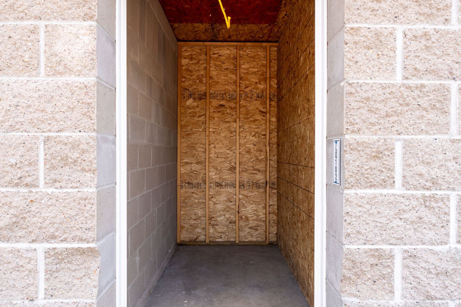 Empty storage unit with plywood walls and concrete floor illuminated by overhead lighting.
