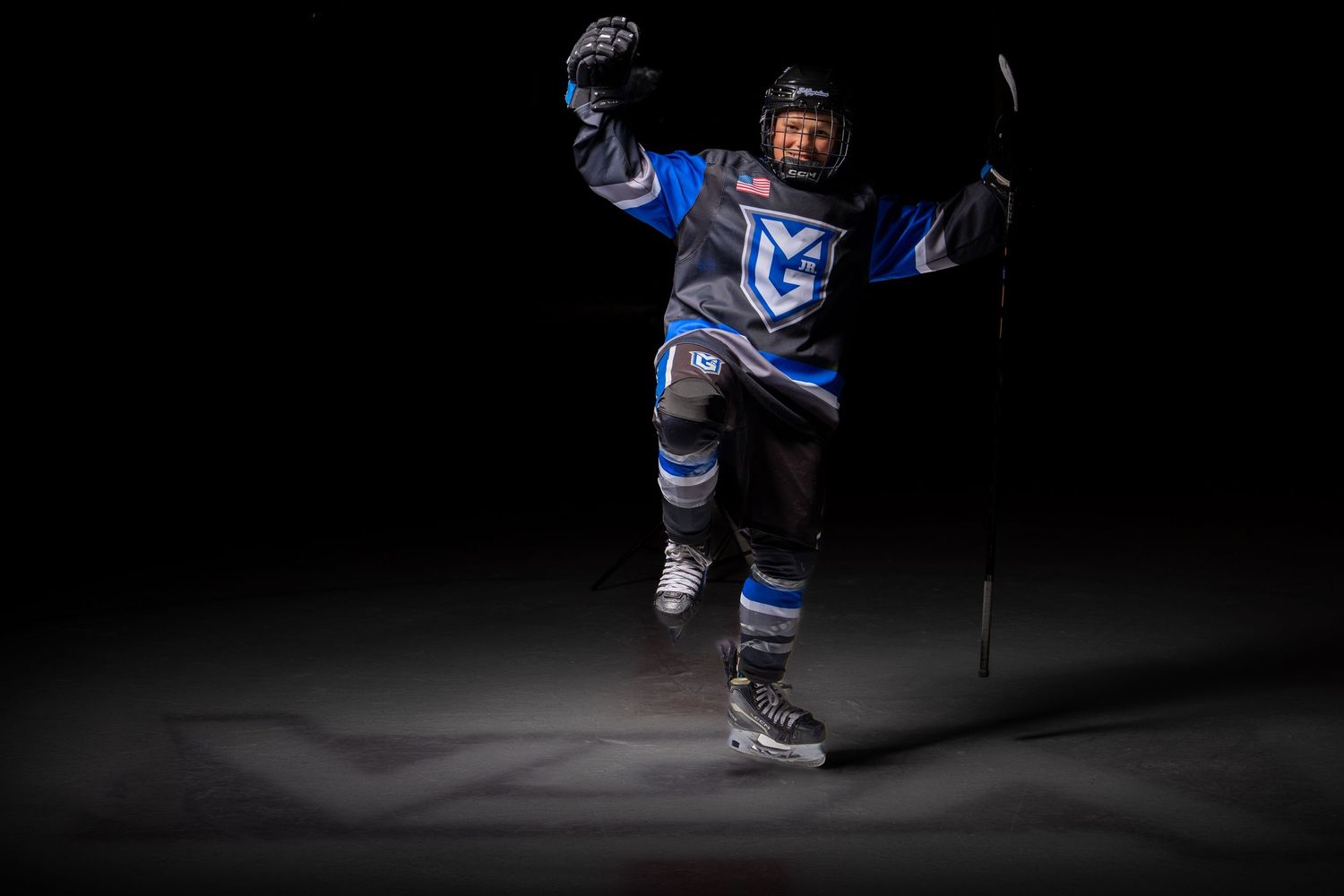 Hockey player in blue uniform celebrates with raised arms on dark ice rink.