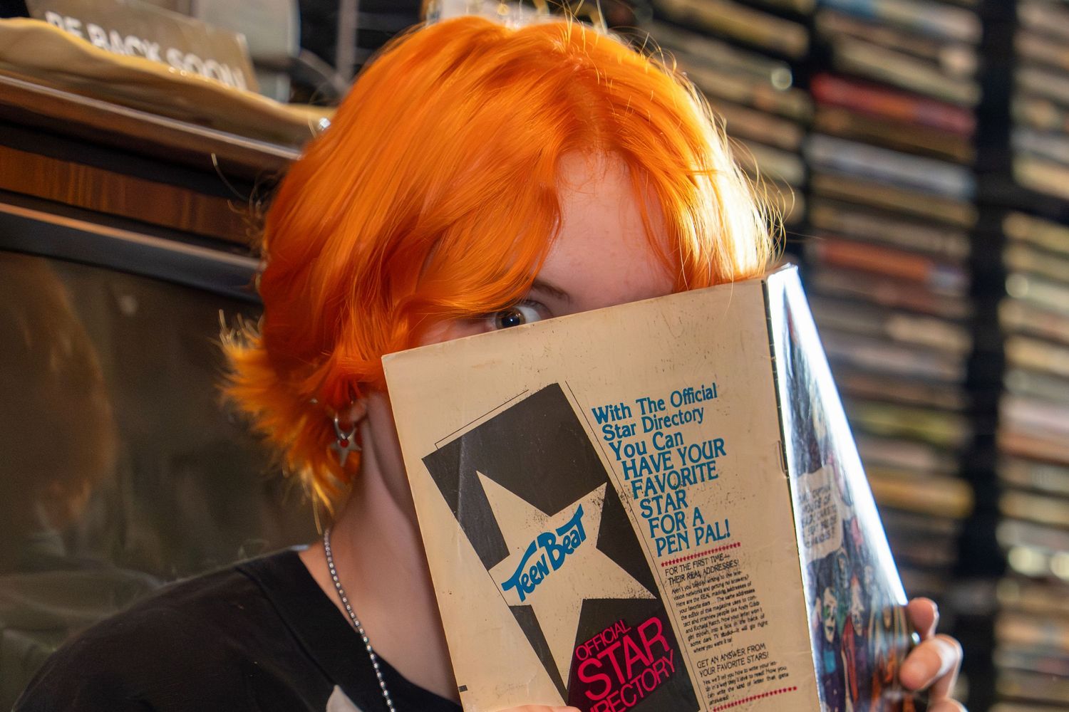 Person with bright orange hair reading a book in front of a wall of bookshelves.