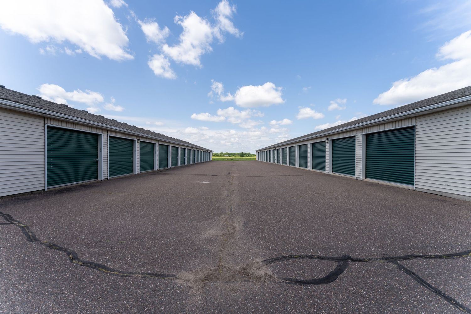 Exterior view of white and green self storage units with metal doors arranged in rows under a blue sky with white clouds.