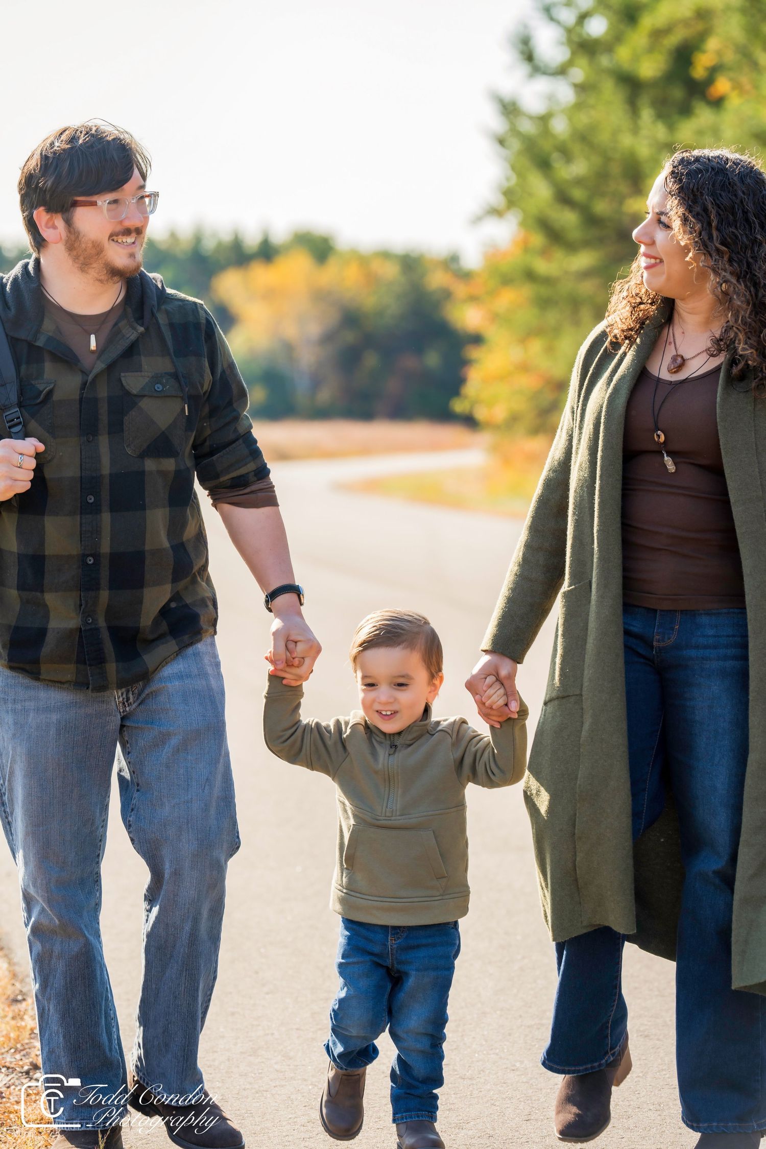 Family walking together on path surrounded by autumn colors and holding hands.