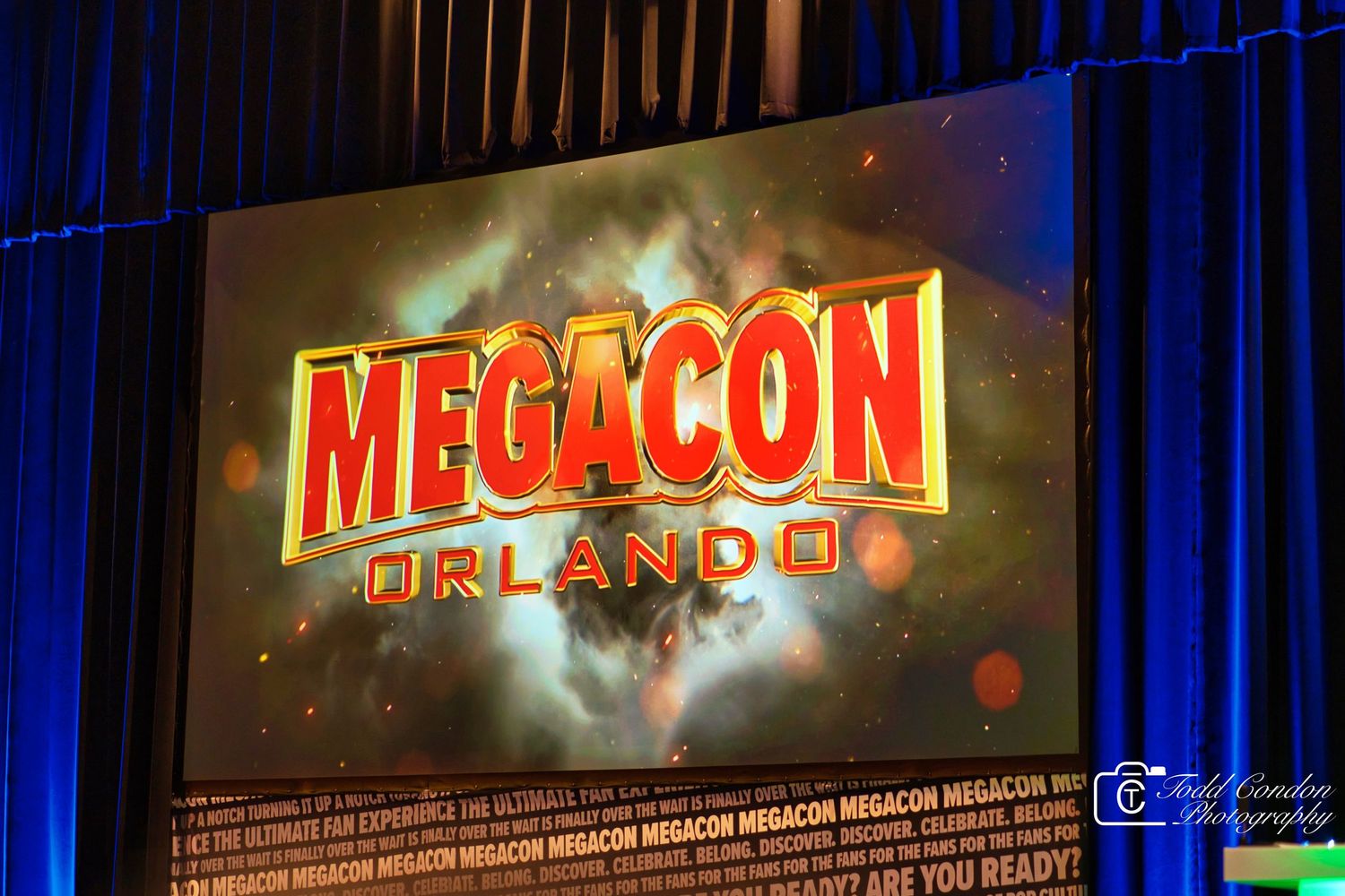 Illuminated Megacon event signage glows brightly against a dark blue curtained background at a convention center.