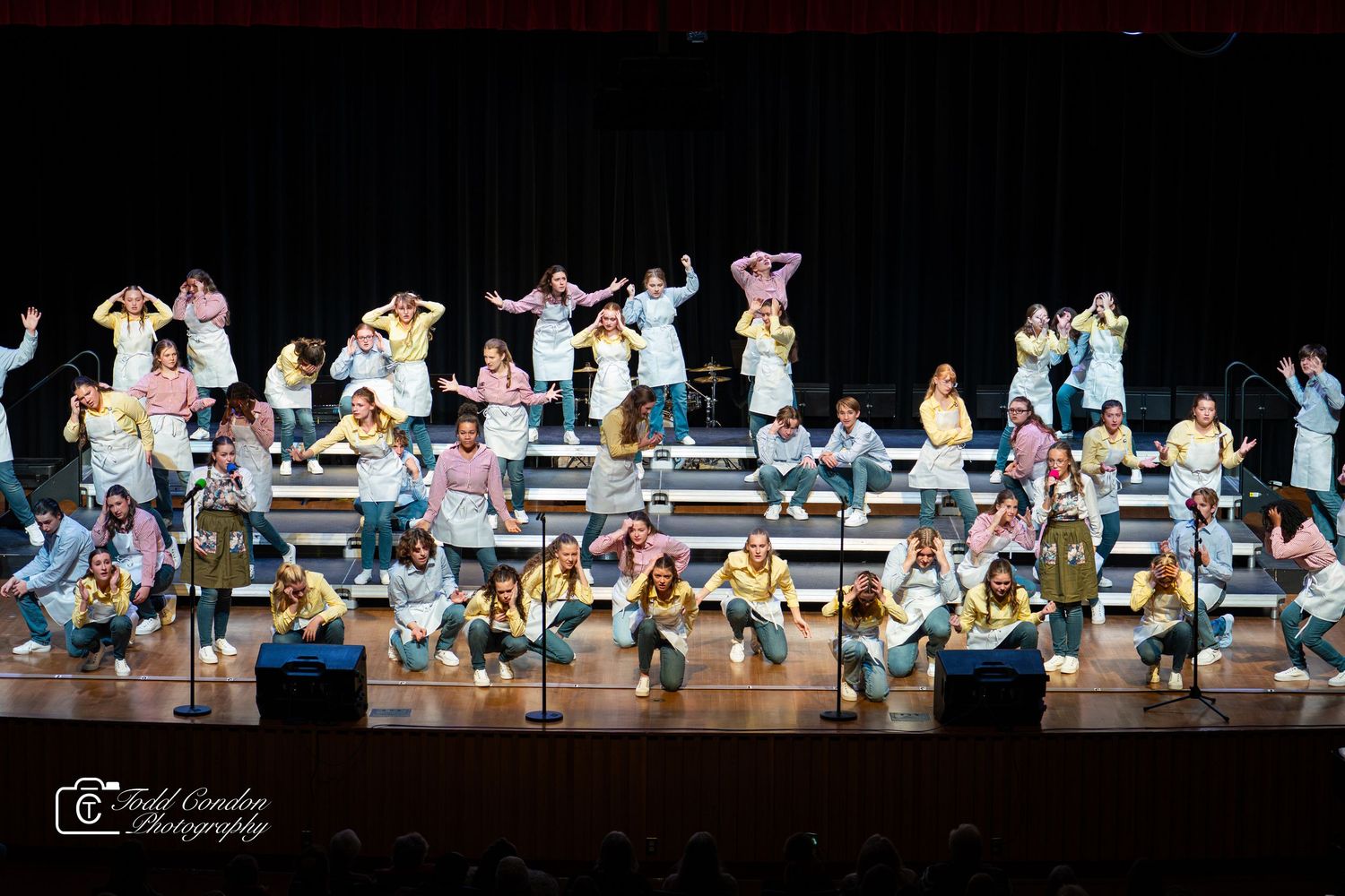 Dancers in colorful costumes perform a synchronized routine on stage during a theatrical production.