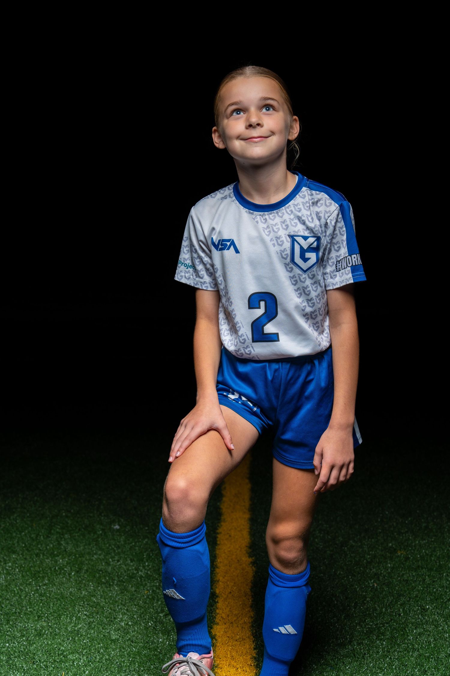 Youth soccer player in blue and white uniform poses confidently on artificial turf field.