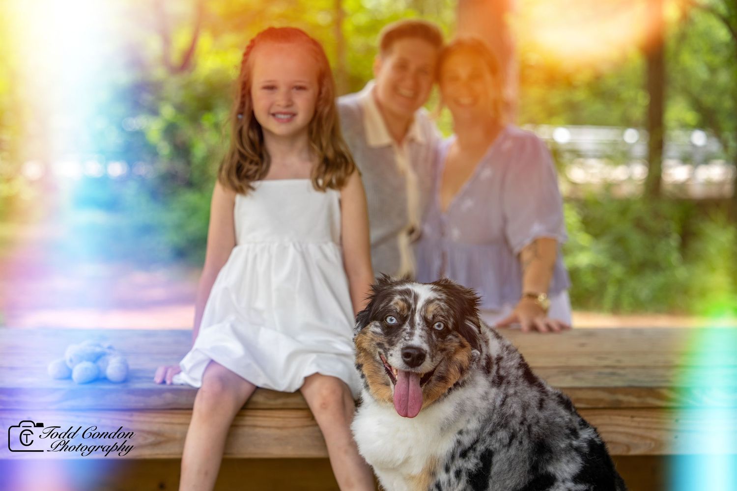 A happy family and their Australian Shepherd dog pose together with rainbow light effects.
