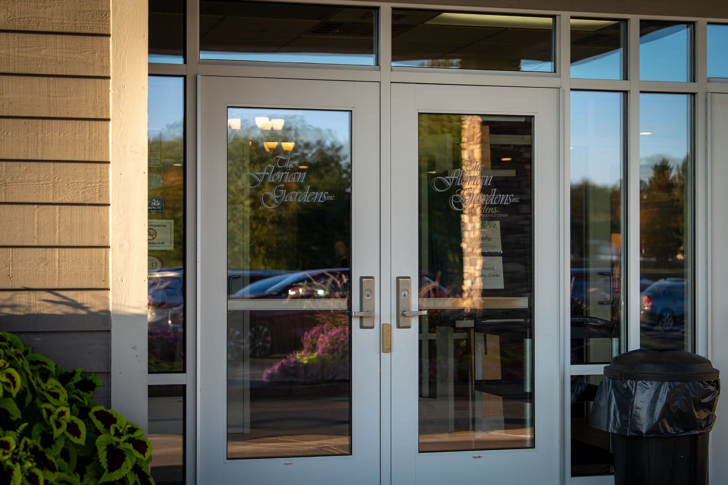 Glass storefront entrance of a commercial building with tan siding and large windows reflecting sunlight.